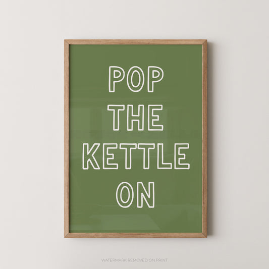 A framed typographic wall art print with the phrase “POP THE KETTLE ON” in white outlined letters on an olive green background, shown hanging against a light neutral wall.