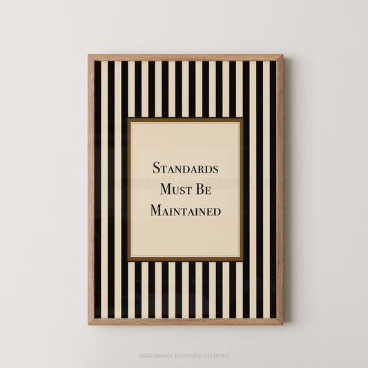 Framed wall art print with vertical black and cream stripes, a central cream panel, and the text 'STANDARDS MUST BE MAINTAINED' in black serif lettering, shown against a light neutral wall.