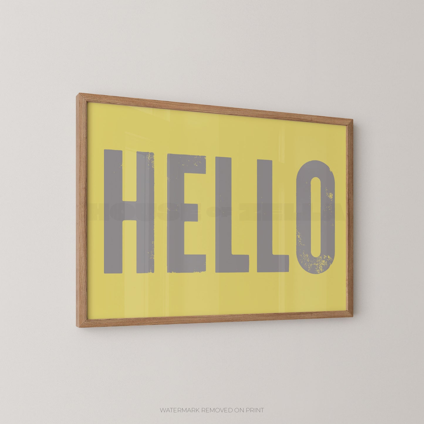 Framed wall art print with the word "HELLO" in large gray letters on a yellow background, shown hanging on a light gray wall.