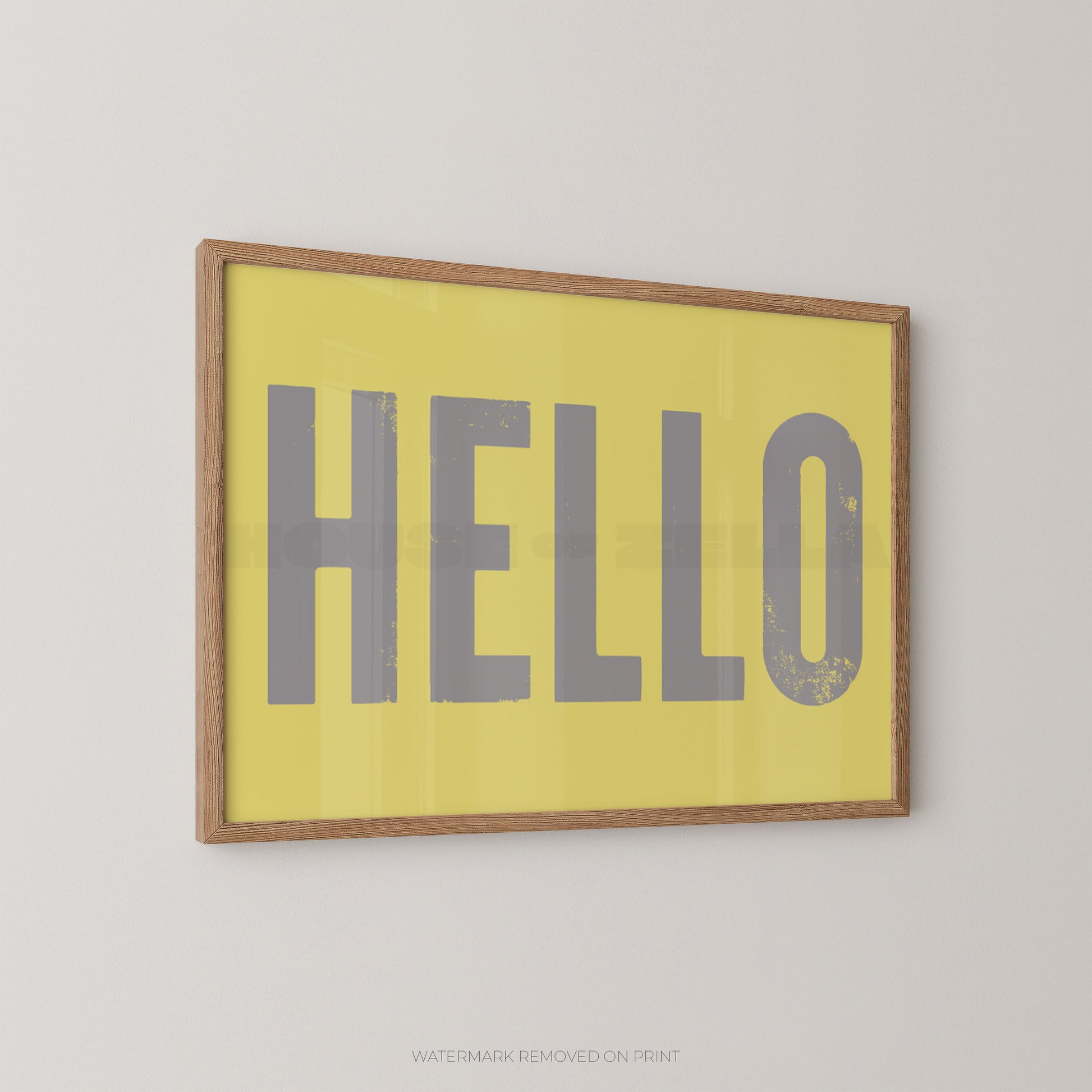 Framed wall art print with the word "HELLO" in large gray letters on a yellow background, shown hanging on a light gray wall.
