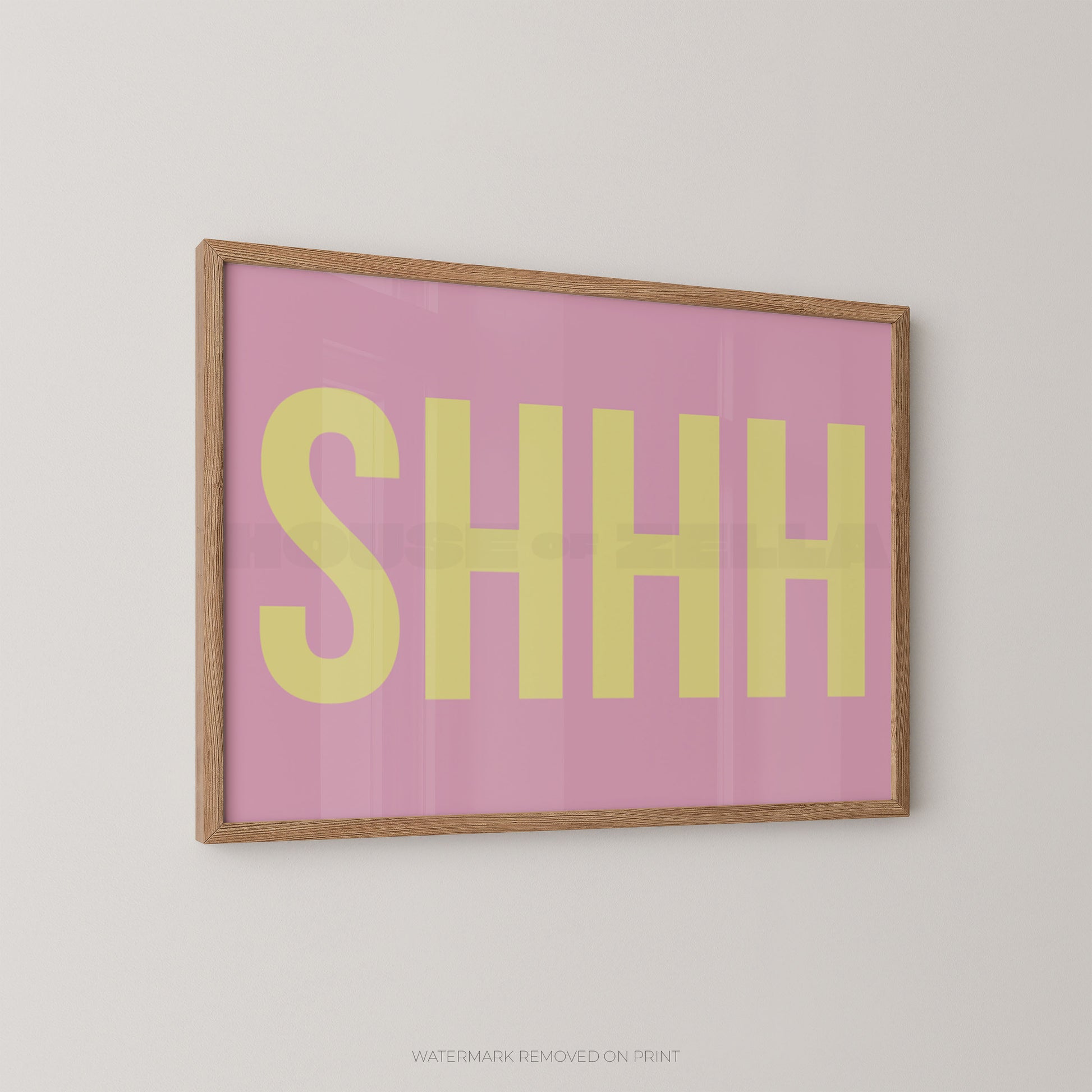 Framed typographic wall art featuring the word 'SHHH' in large yellow letters on a pink background, shown hanging on a light gray wall.