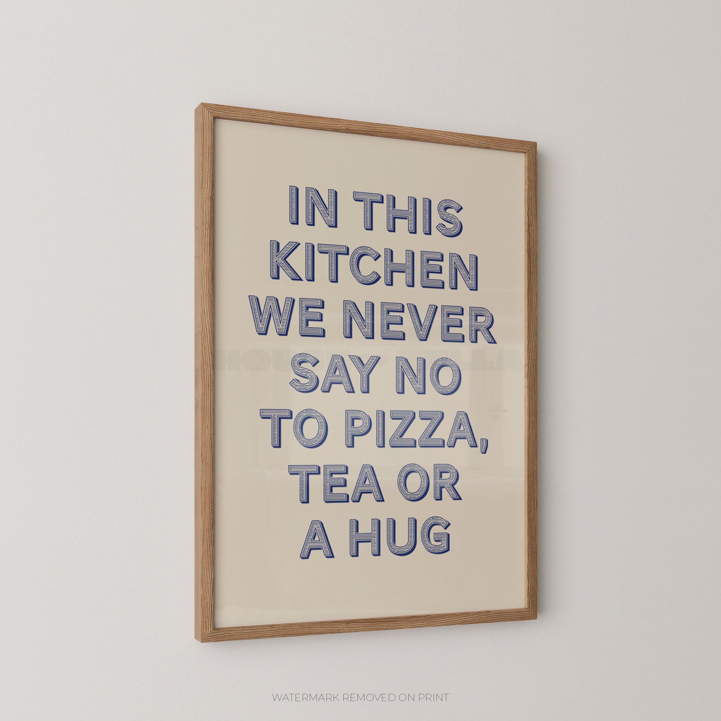 Framed typographic wall art hanging on a light wall, with a light wood frame and raised blue text reading, 'IN THIS KITCHEN WE NEVER SAY NO TO PIZZA, TEA OR A HUG.'.