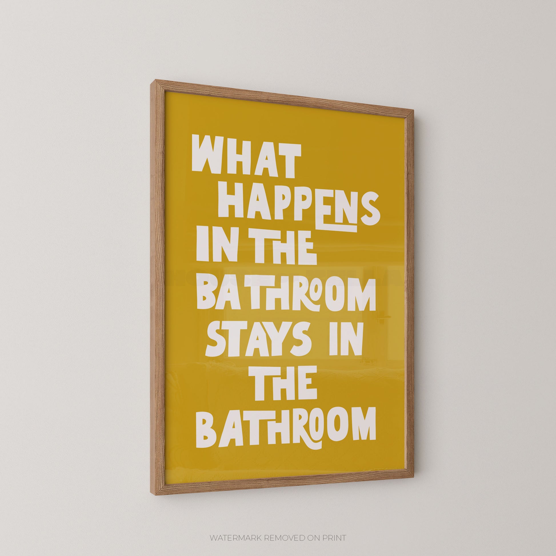 Funny bathroom wall art print in a wood frame – playful chunky cream typography on a yellow background reading "What Happens In The Bathroom Stays In The Bathroom"