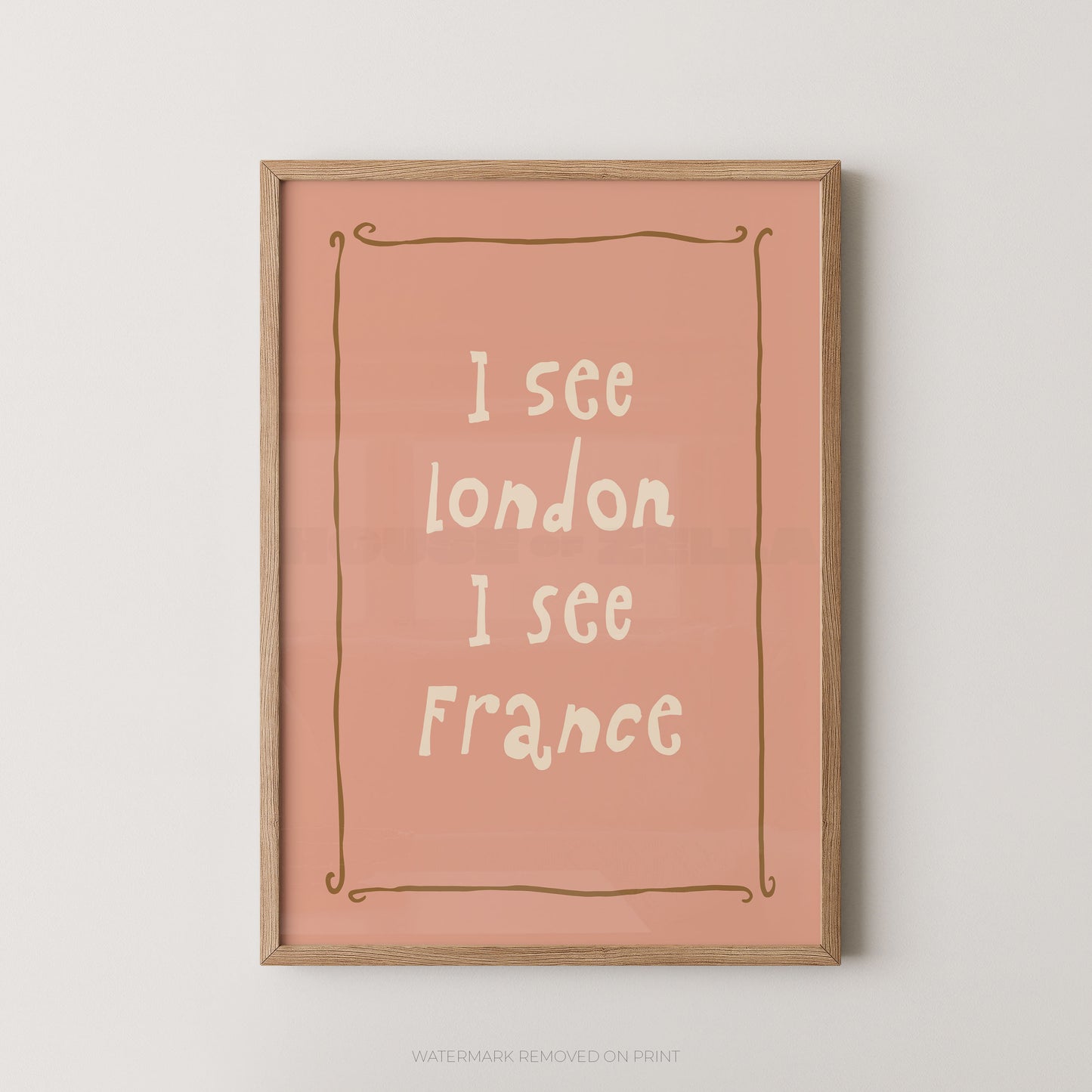 Framed wall art print with the text 'I see London I see France' in white lettering on a dusty pink background, enclosed in a light wood frame and shown against a light gray wall.