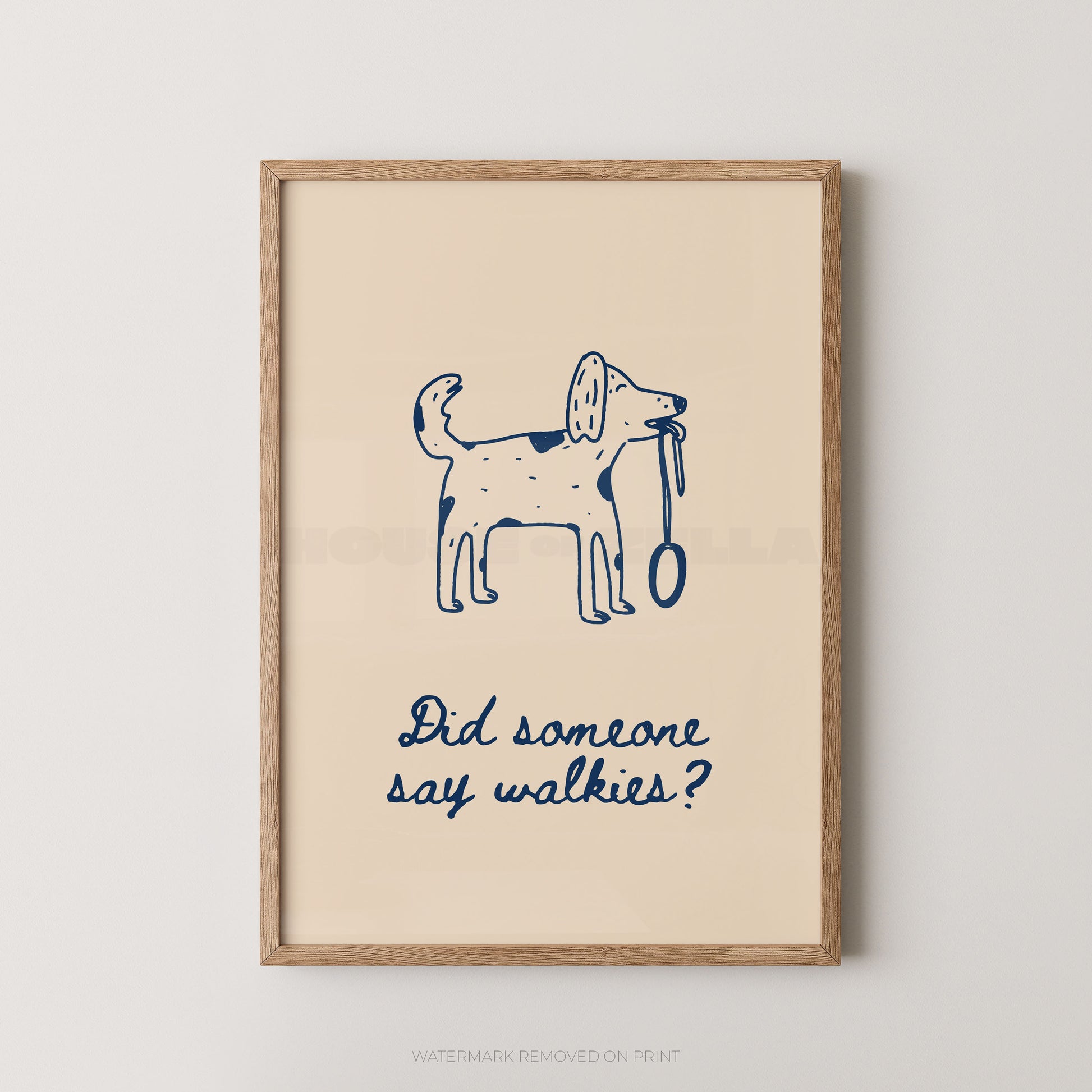 Framed wall art print with a simple navy line drawing of a dog holding a leash and the phrase 'Did someone say walkies?' on a warm cream background, shown in a light wood frame against a light neutral wall.