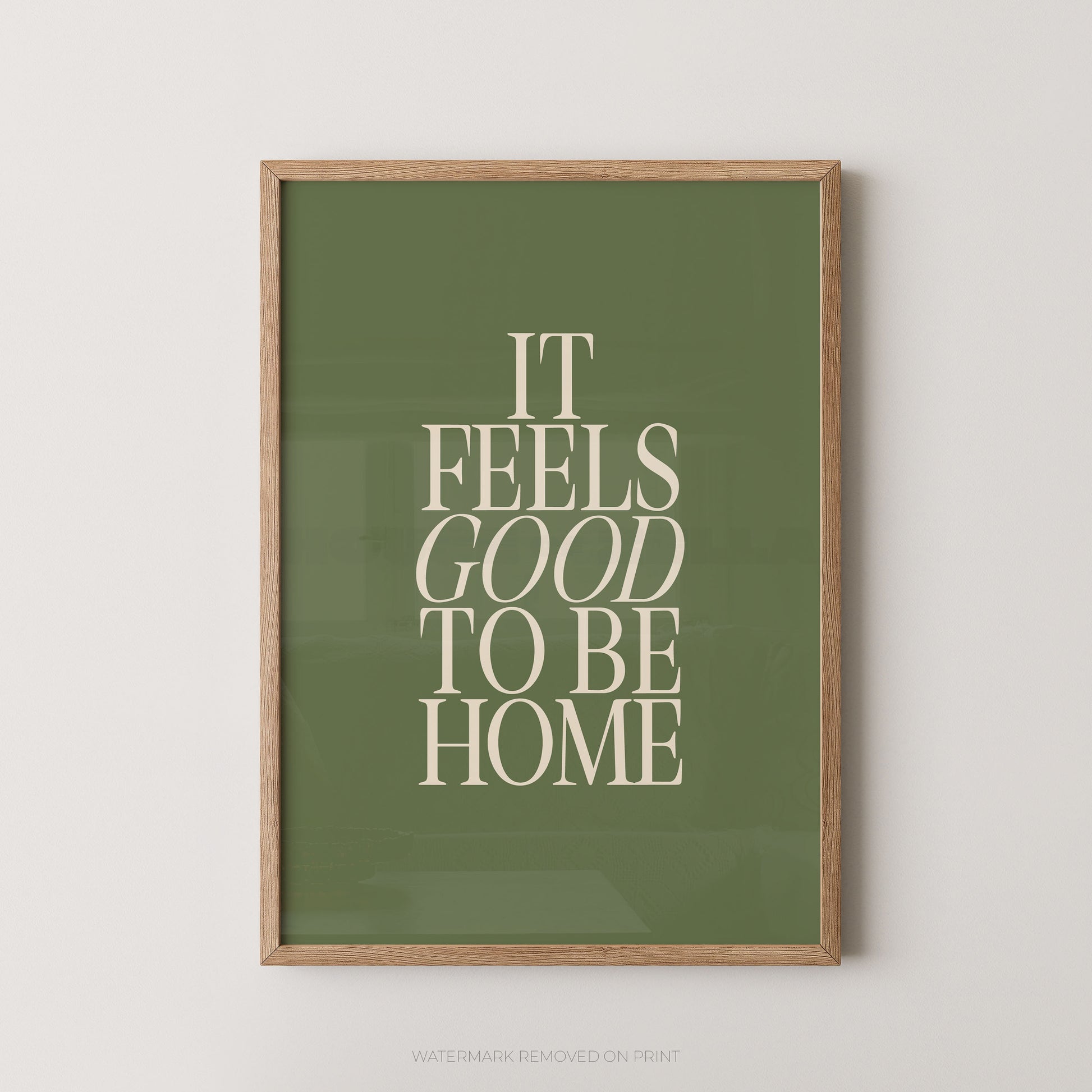 "It Feels Good To Be Home typography wall art print with elegant serif lettering in cream on an olive green background, displayed straight-on in an oak frame"

