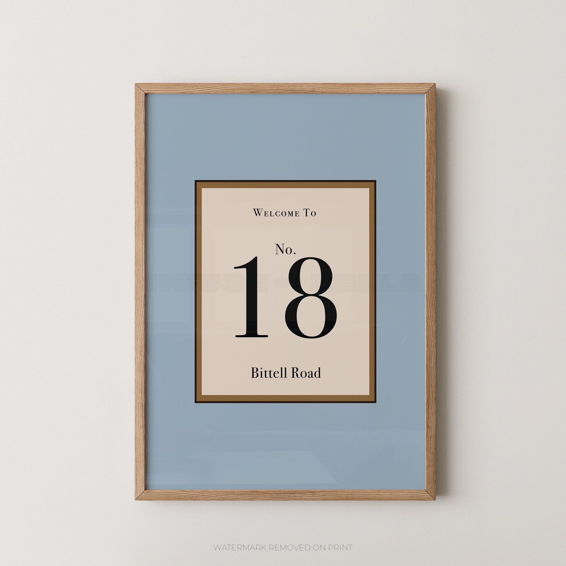 Framed wall art print with a light blue background and a central cream panel reading 'Welcome To No. 18 Bittell Road' in black text, shown in a light wood frame against a white wall.