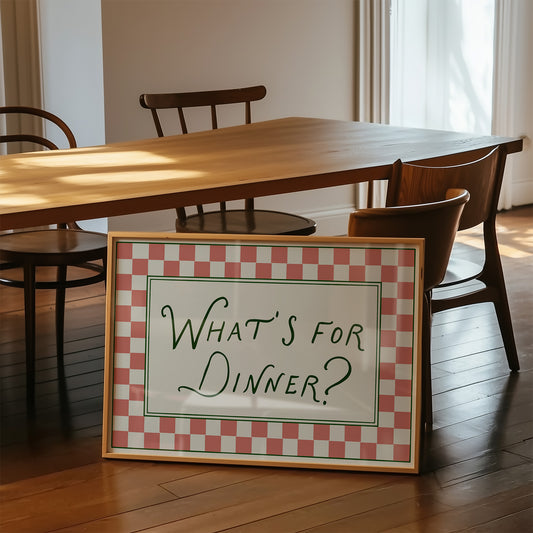 Dining table with chairs and a framed sign asking 'What's for Dinner?' on a wooden floor.