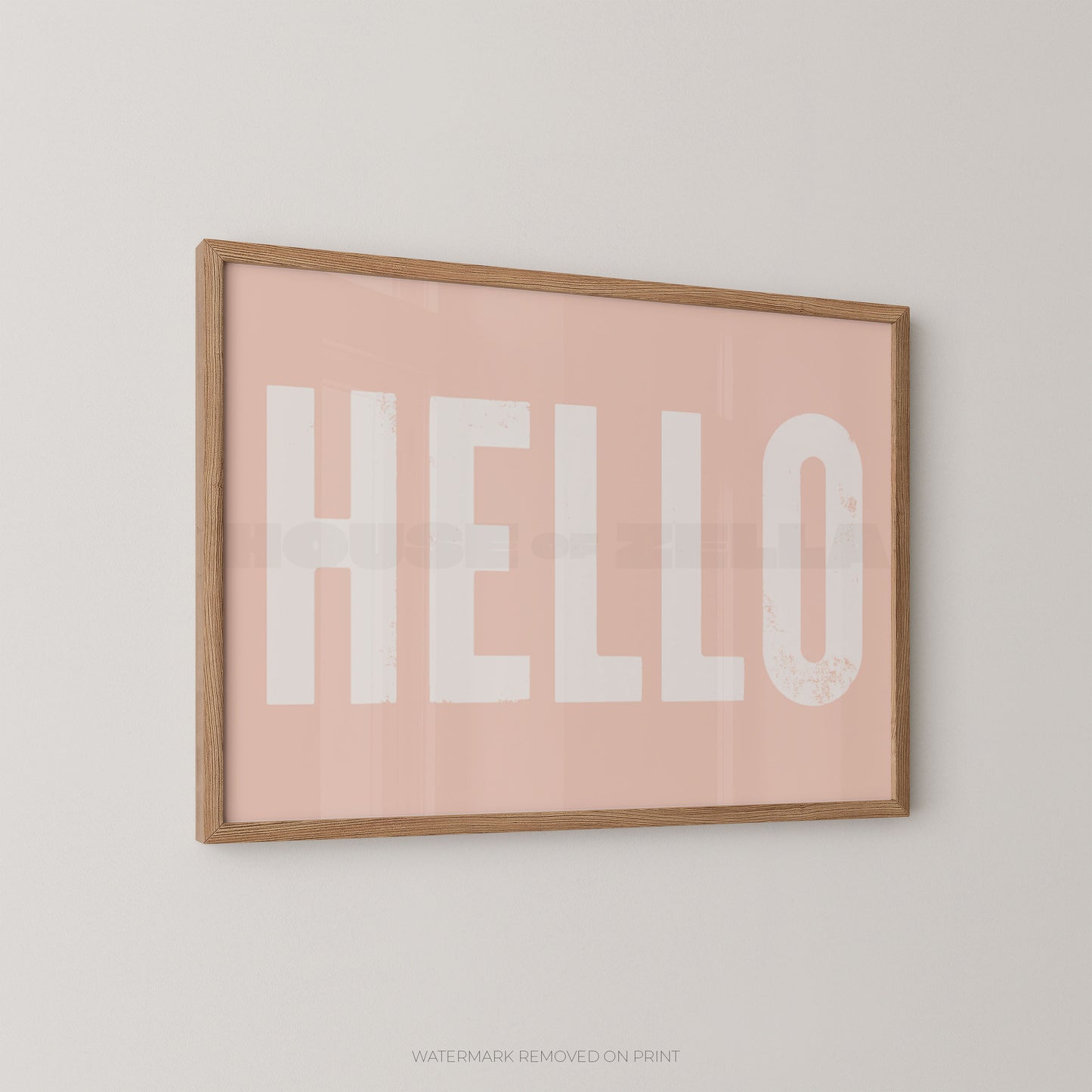 Framed wall art print with the word "HELLO" in large white letters on a soft pink background, shown hanging on a light neutral wall.