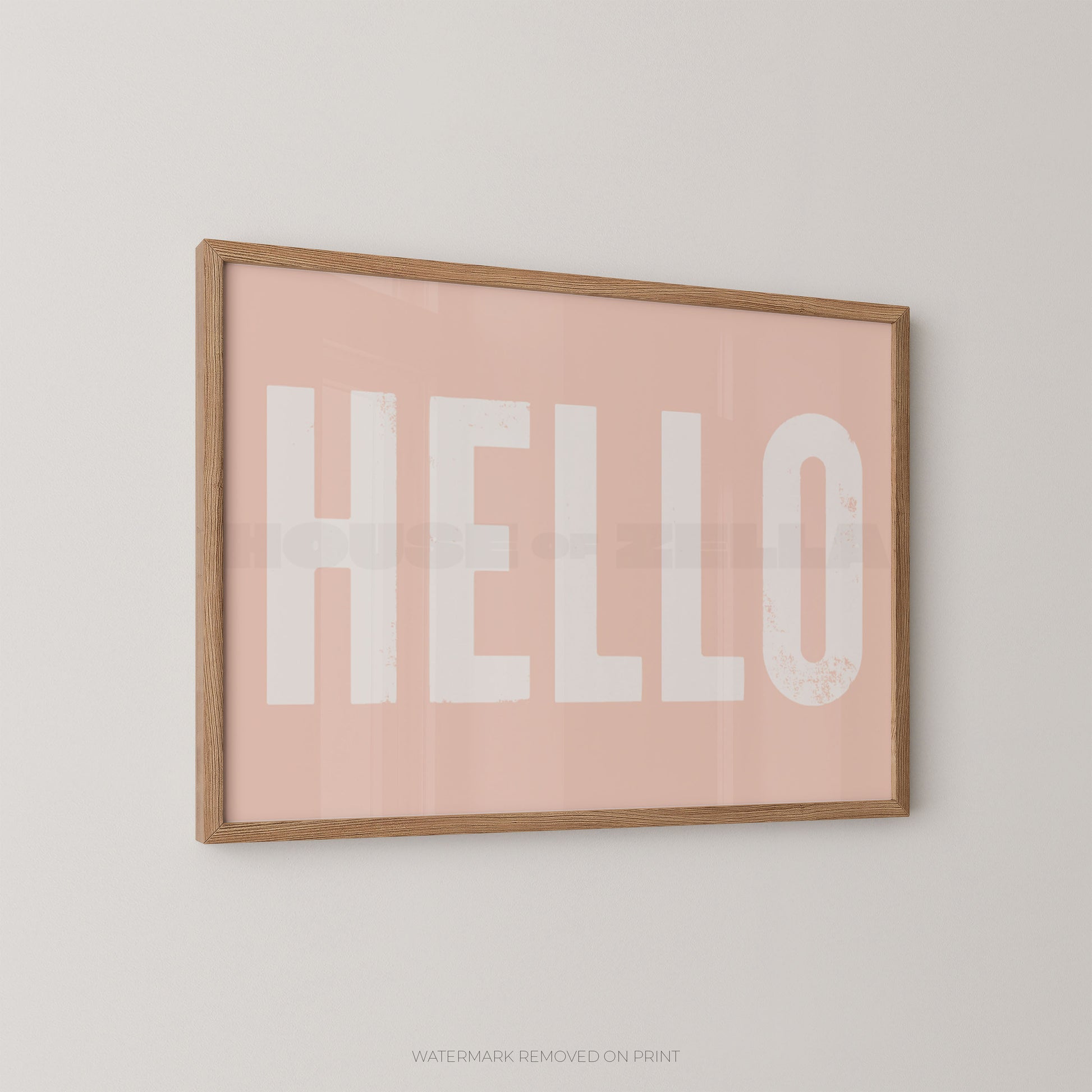 Framed wall art print with the word "HELLO" in large white letters on a soft pink background, shown hanging on a light neutral wall.