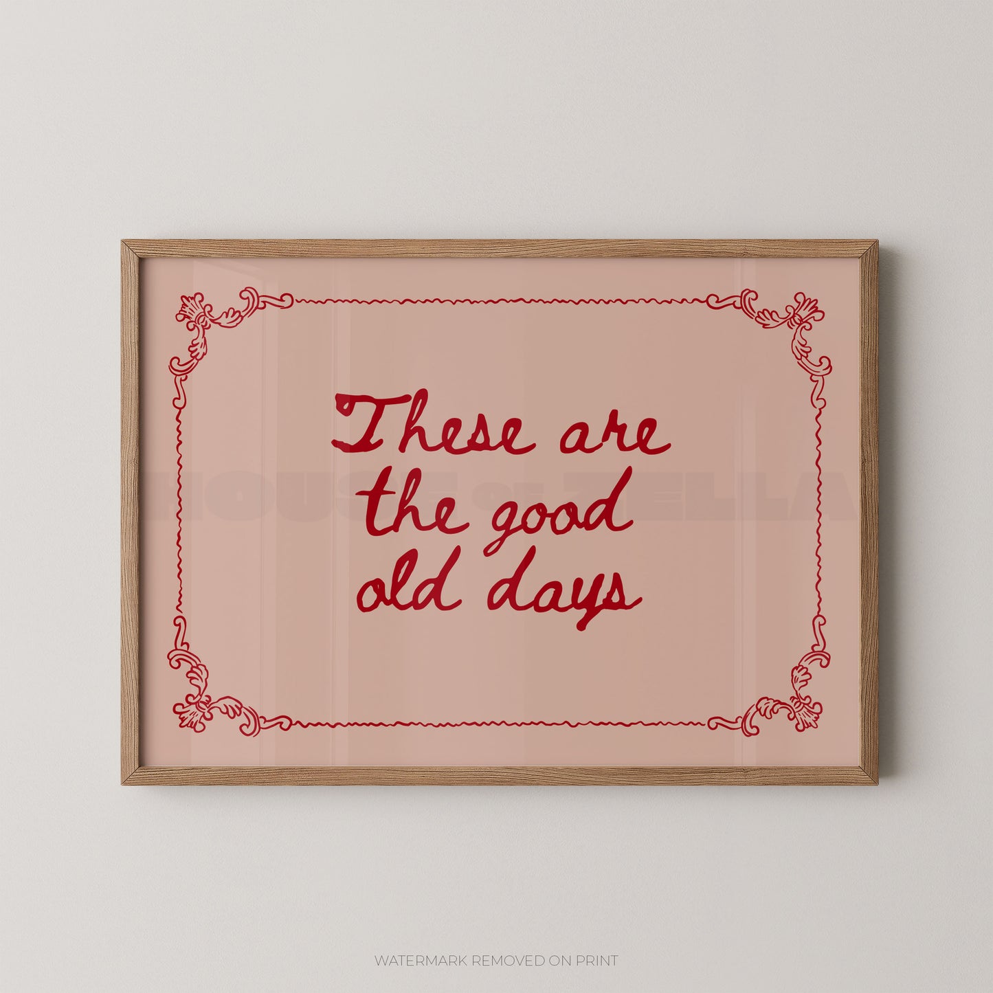 Framed wall art print with the phrase “These are the good old days” in red script inside a light wood frame, shown against a plain light gray wall.