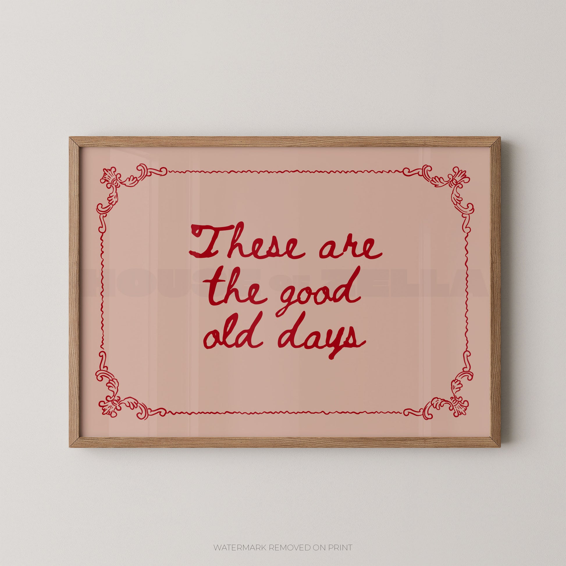 Framed wall art print with the phrase “These are the good old days” in red script inside a light wood frame, shown against a plain light gray wall.