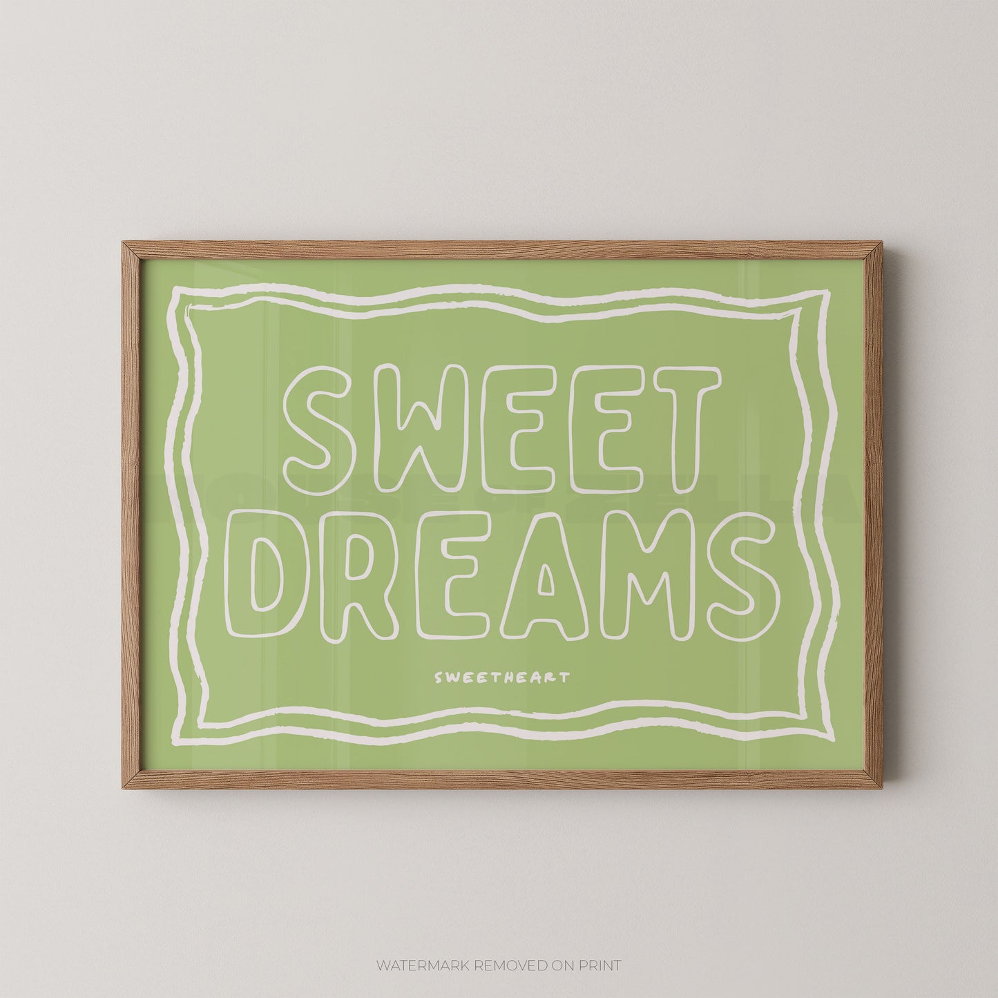 A framed wall art print with the words “SWEET DREAMS” in large outlined letters on a light green background, enclosed in a natural wood frame and shown against a light gray wall.