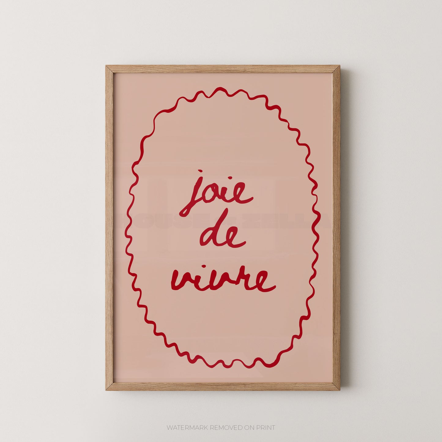 A framed wall art print with the French phrase “joie de vivre” in red script inside a red wavy oval border, set in a light wood frame against a plain light gray wall.