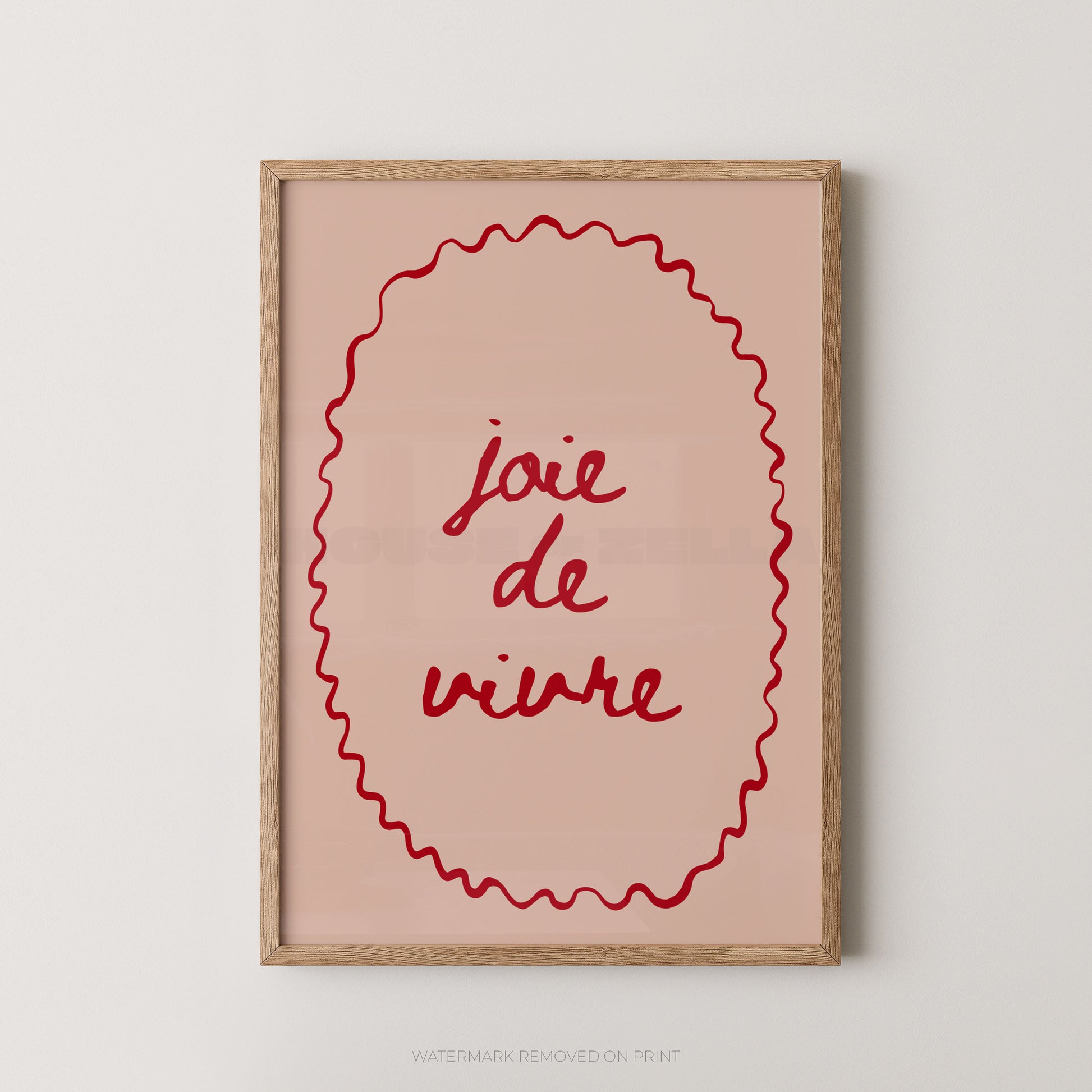 A framed wall art print with the French phrase “joie de vivre” in red script inside a red wavy oval border, set in a light wood frame against a plain light gray wall.
