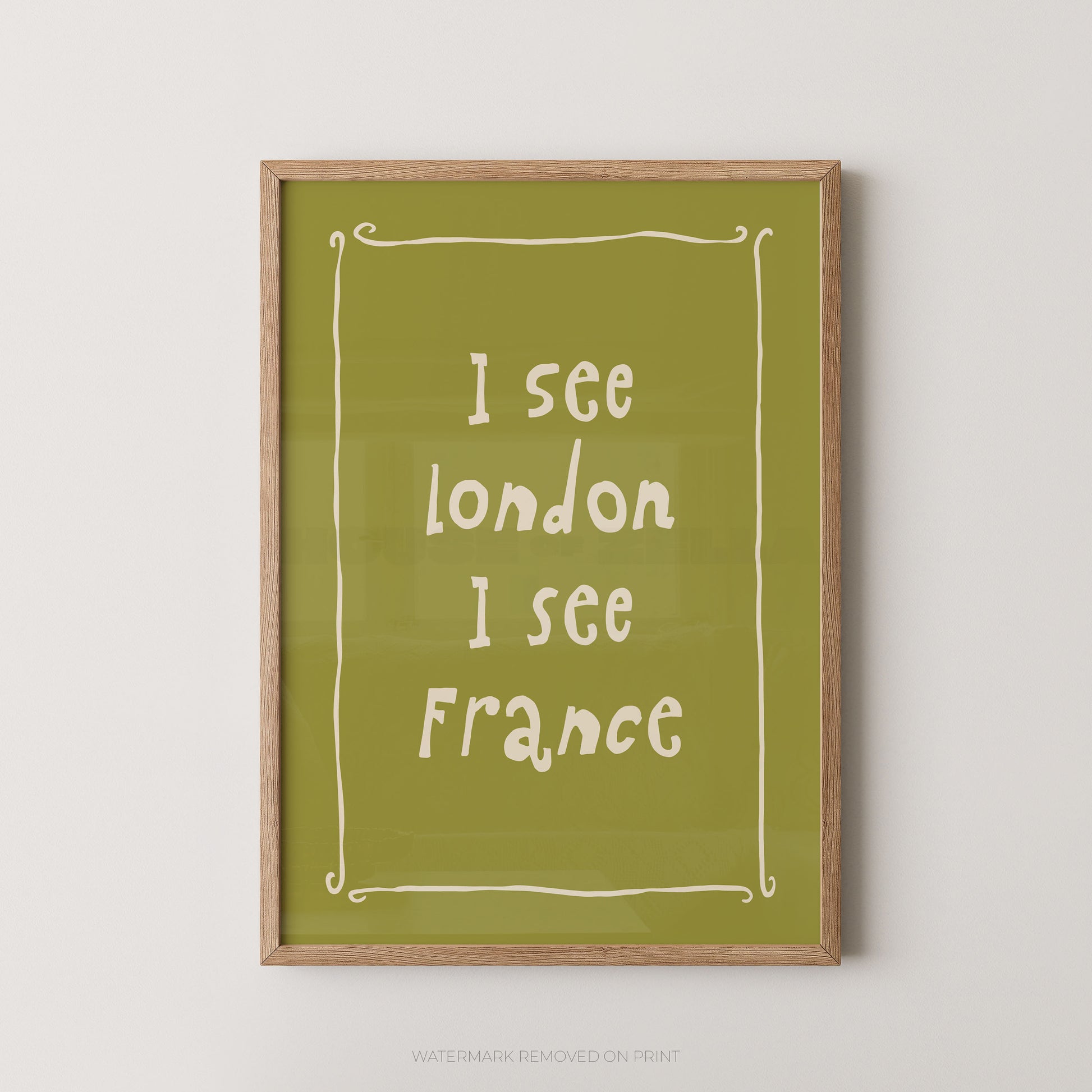 Framed wall art print with the phrase 'I see london I see France' in white handwritten-style text on an olive green background, shown in a light wood frame against a plain light wall.