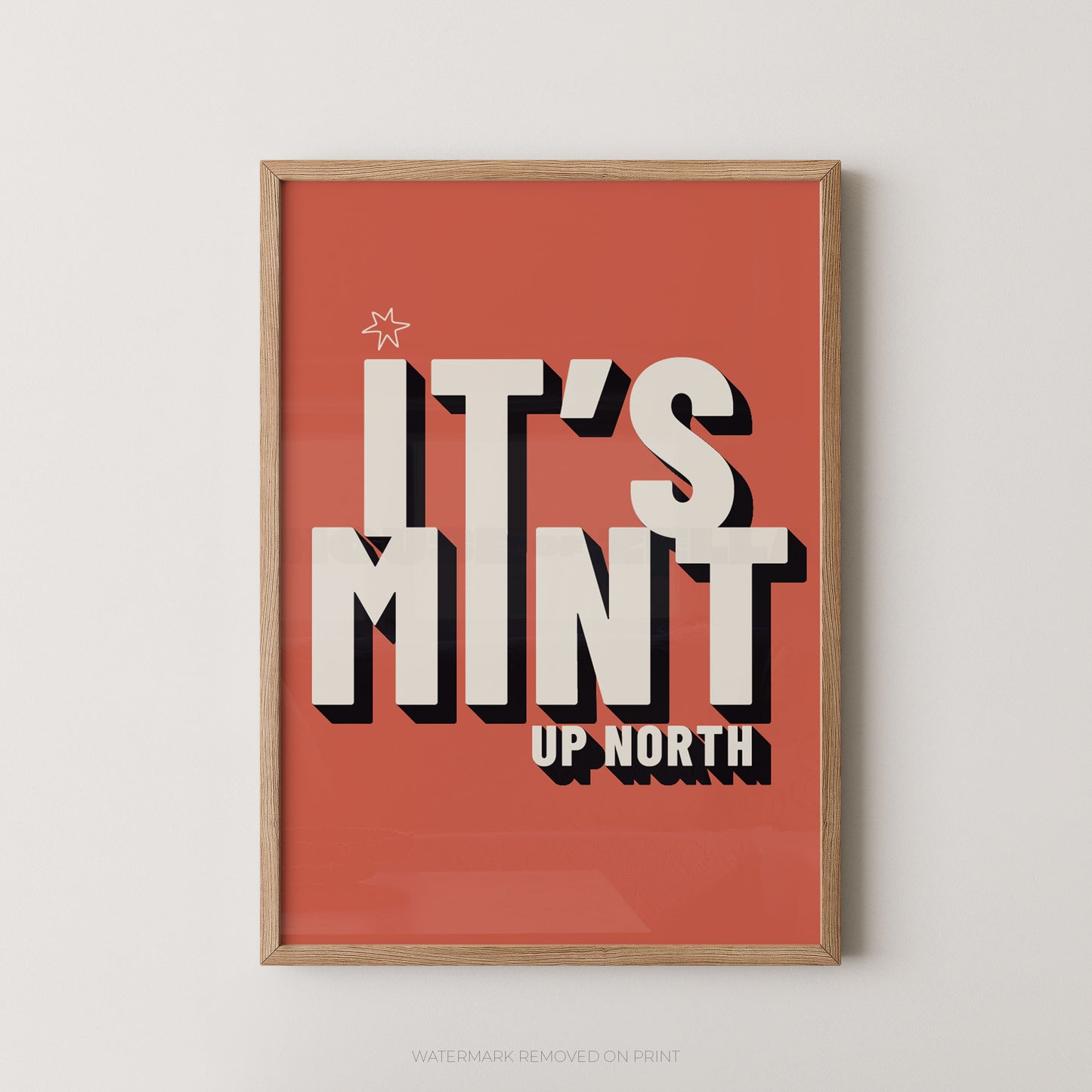 Framed typographic wall art hanging on a light neutral wall. The print has a striking red background with large cream lettering reading “IT’S MINT” and smaller cream text reading “UP NORTH,” plus a small star near the top left.