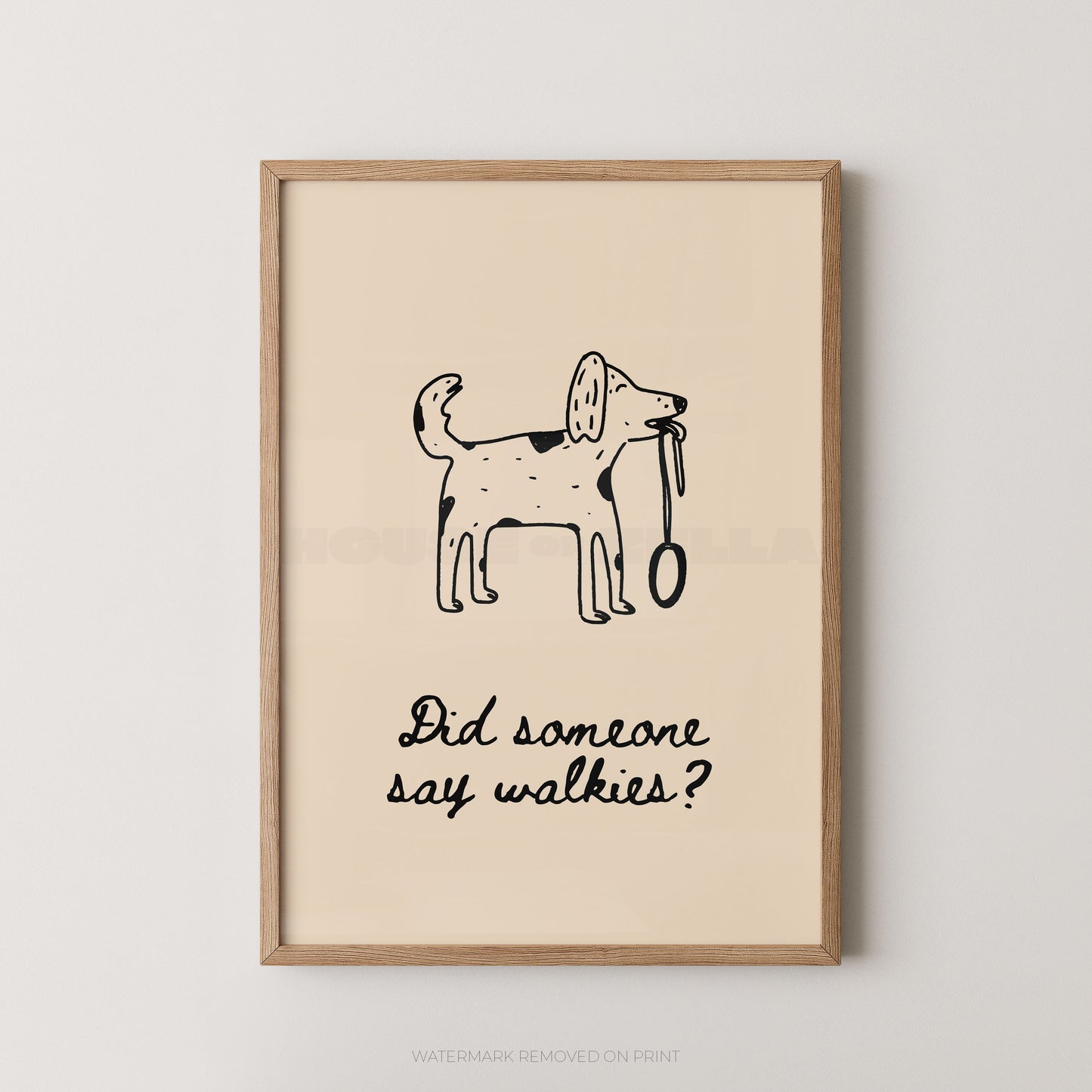 Framed wall art print with a simple black line drawing of a dog holding a leash and the text 'Did someone say walkies?' on a warm cream background, shown in a light wood frame against a light gray wall.