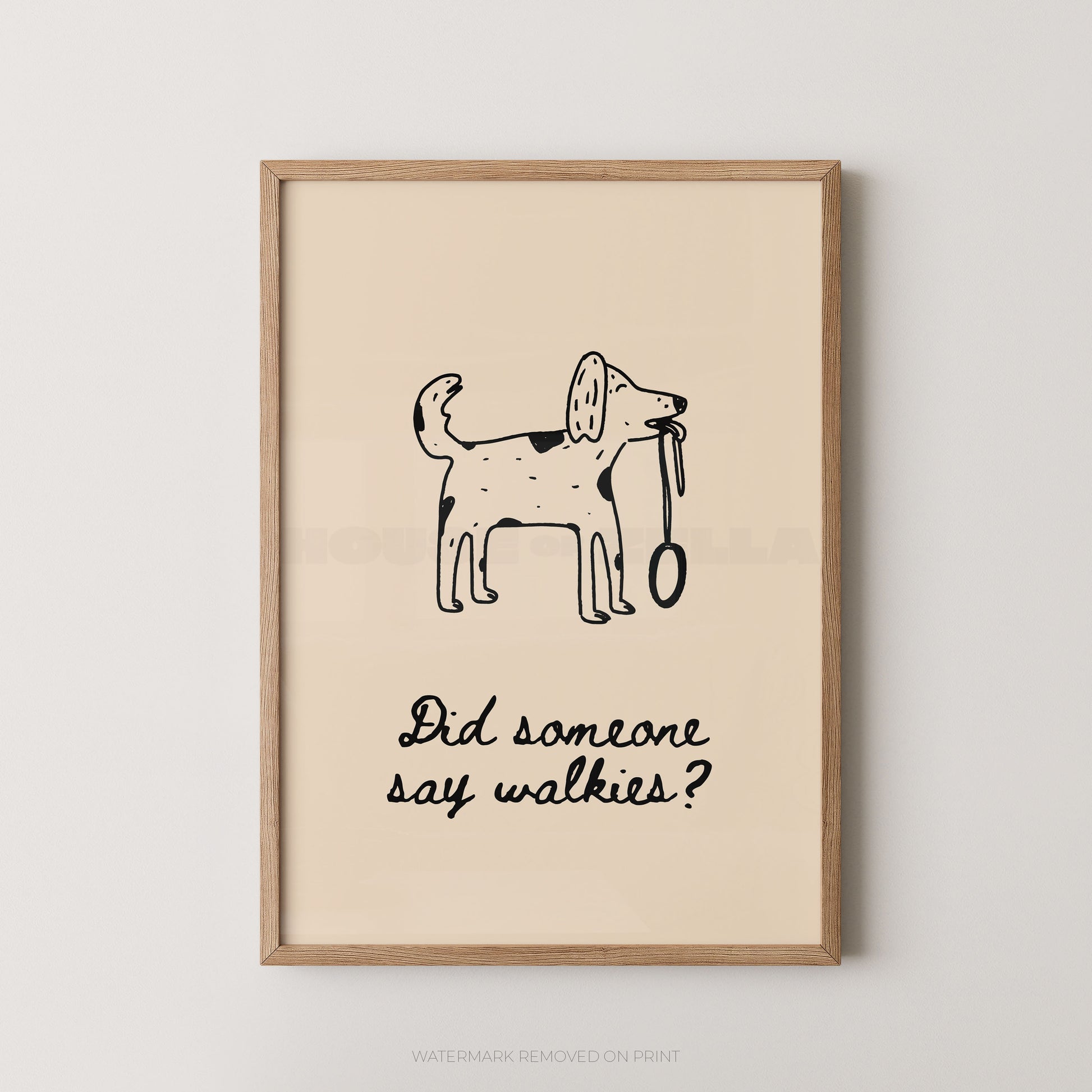 Framed wall art print with a simple black line drawing of a dog holding a leash and the text 'Did someone say walkies?' on a warm cream background, shown in a light wood frame against a light gray wall.