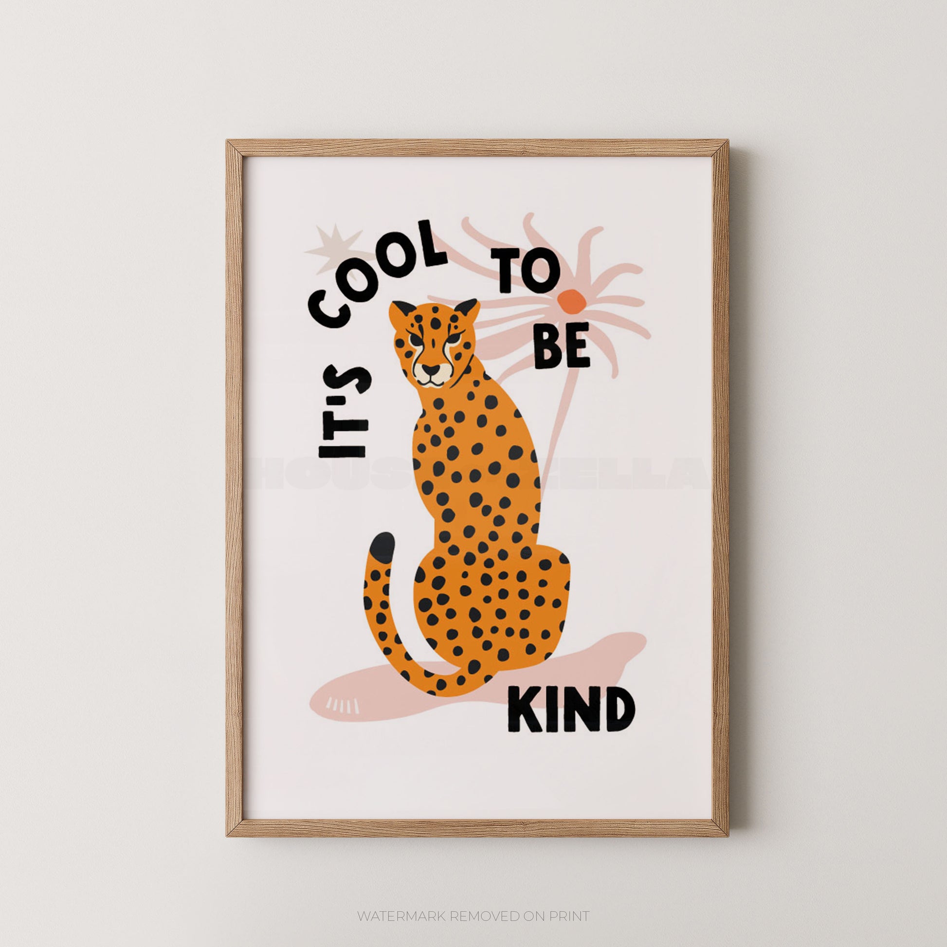 Framed wall art featuring an illustrated orange-and-black spotted cat sitting in front of palm trees, with the text 'IT'S COOL TO BE KIND' in black lettering on a white background.