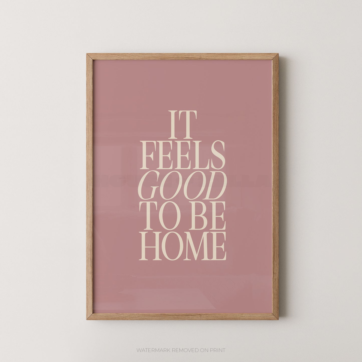 "It Feels Good To Be Home typography wall art print with elegant serif lettering in cream on a dusky pink background, displayed straight-on in an oak frame"

