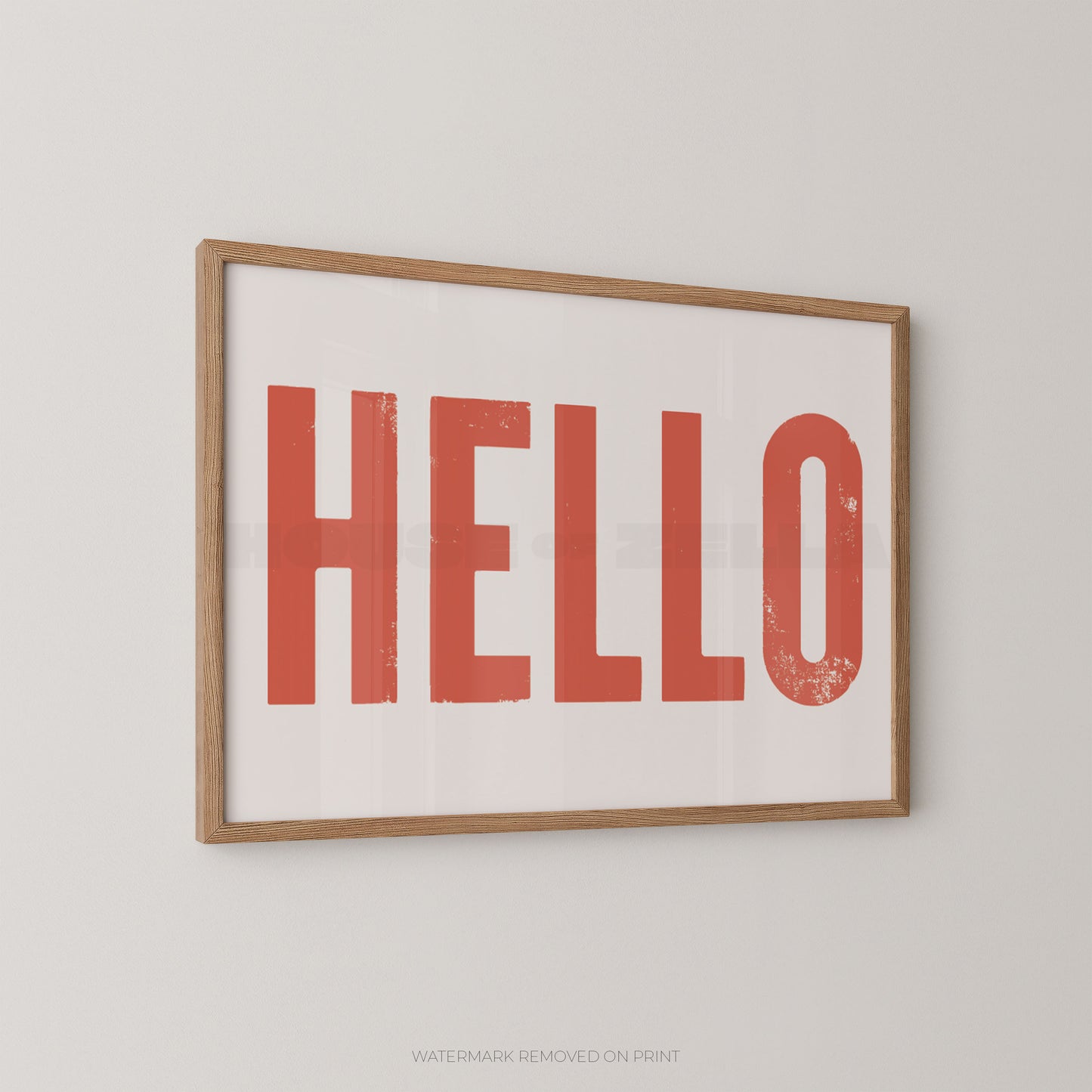 Bold typography wall art print of the word HELLO in distressed red font on a white background, in an oak frame and hung on a white wall.