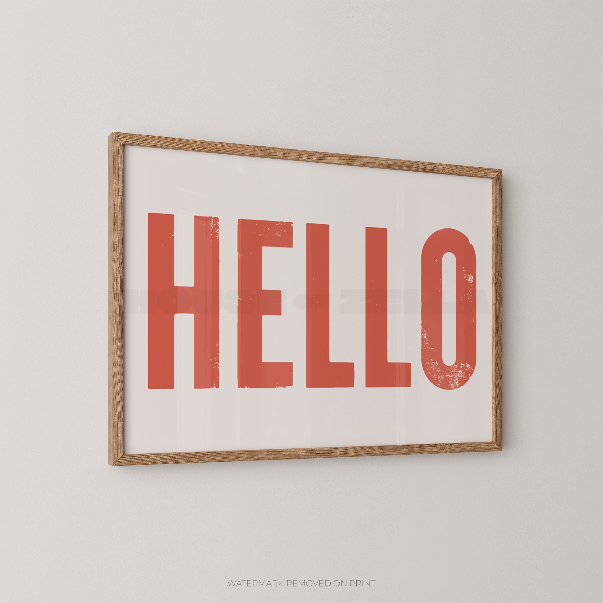 Bold typography wall art print of the word HELLO in distressed red font on a white background, in an oak frame and hung on a white wall.