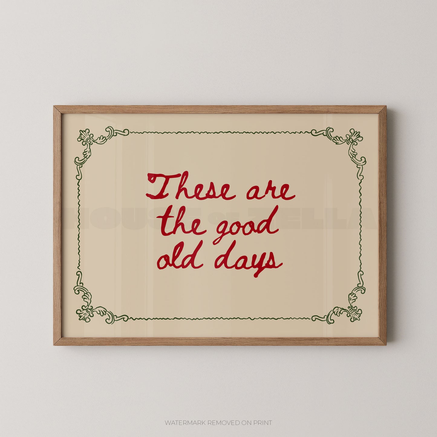 Framed wall art print with the phrase “These are the good old days” in red script inside a light wood frame, shown against a plain light gray wall.