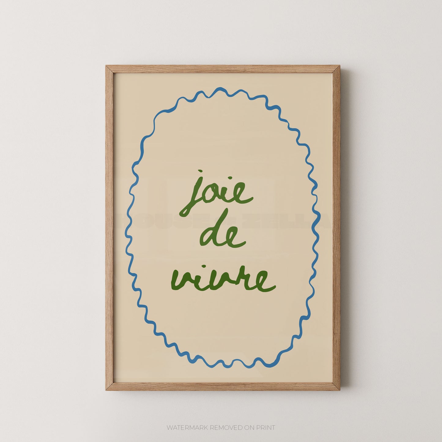 Framed wall art print with the phrase “joie de vivre” in green script inside a blue wavy oval border on a warm cream background, set in a light wood frame against a light gray wall.