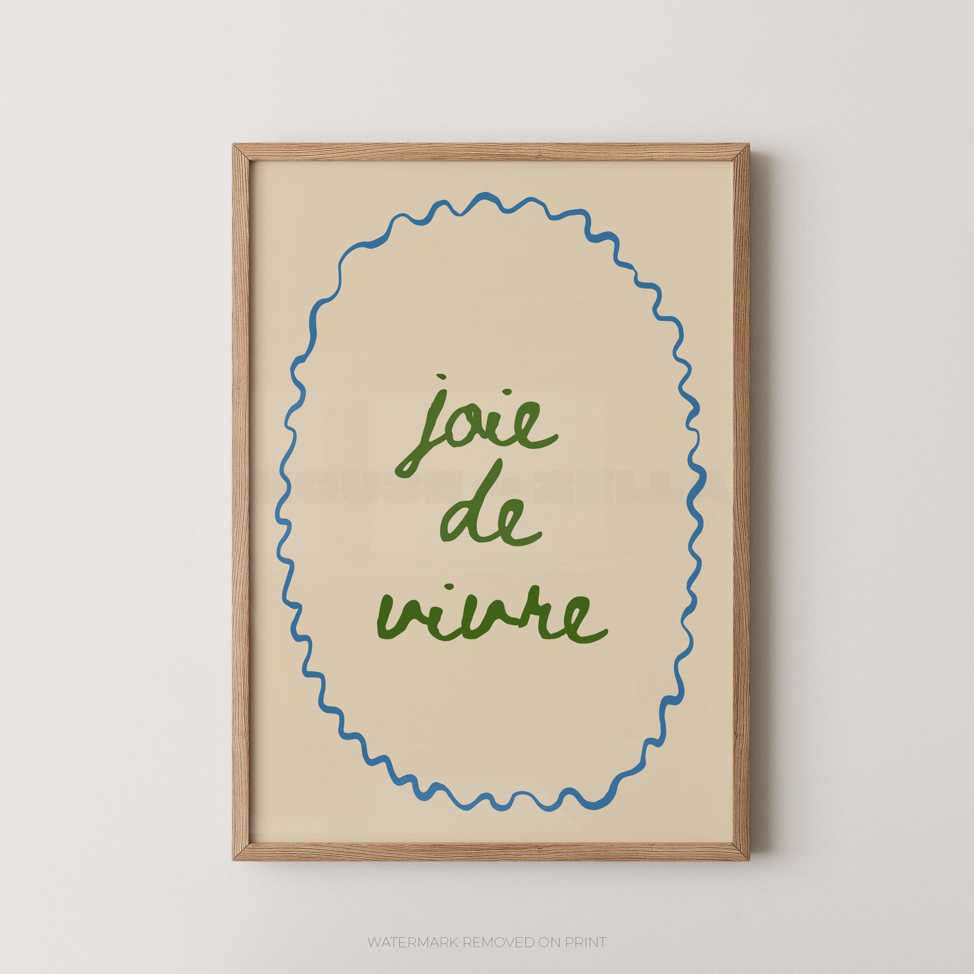 Framed wall art print with the phrase “joie de vivre” in green script inside a blue wavy oval border on a warm cream background, set in a light wood frame against a light gray wall.