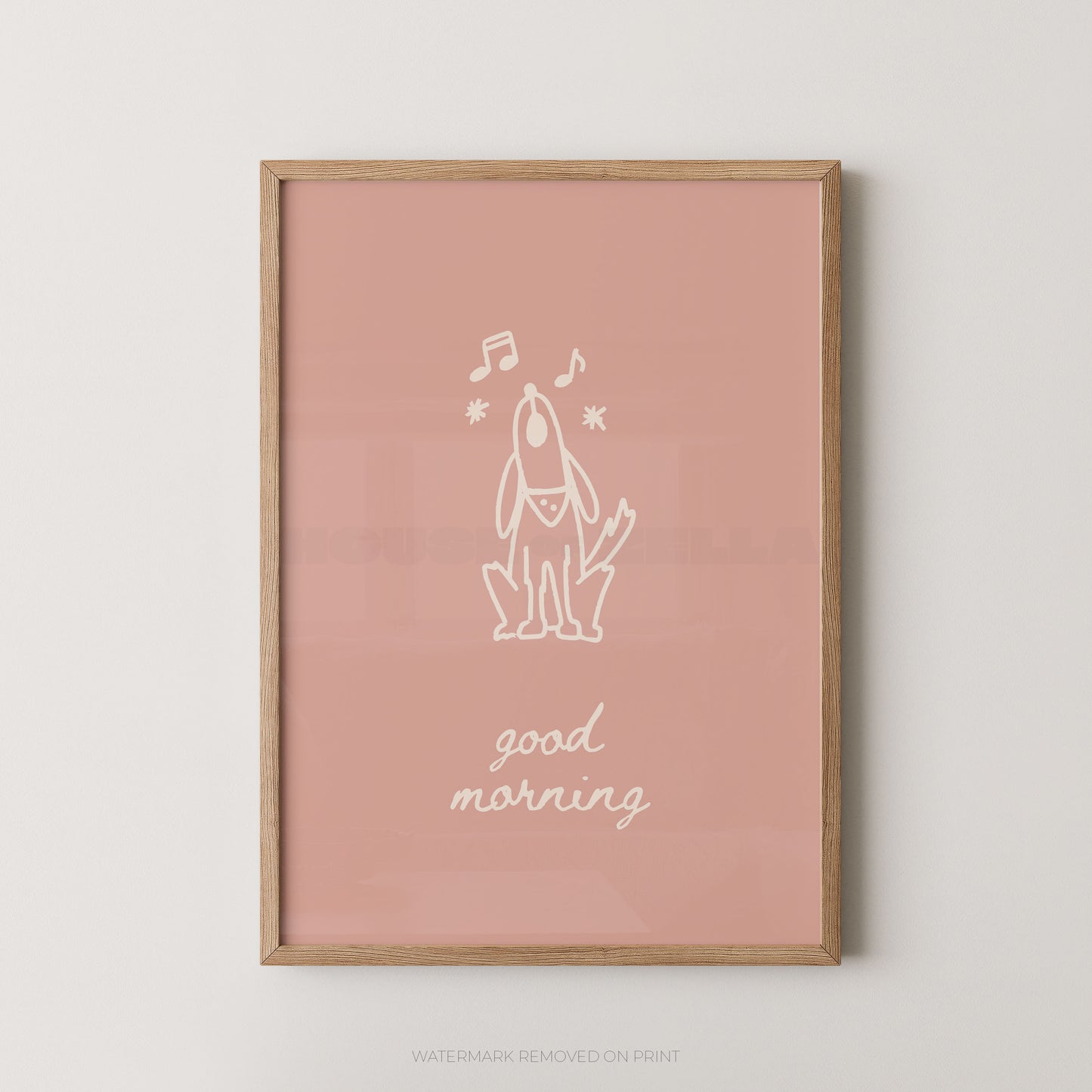 A framed art print featuring a minimalist white line drawing of a dog with musical notes and the text 'good morning' on a dusty pink background, enclosed in a light wood frame.
