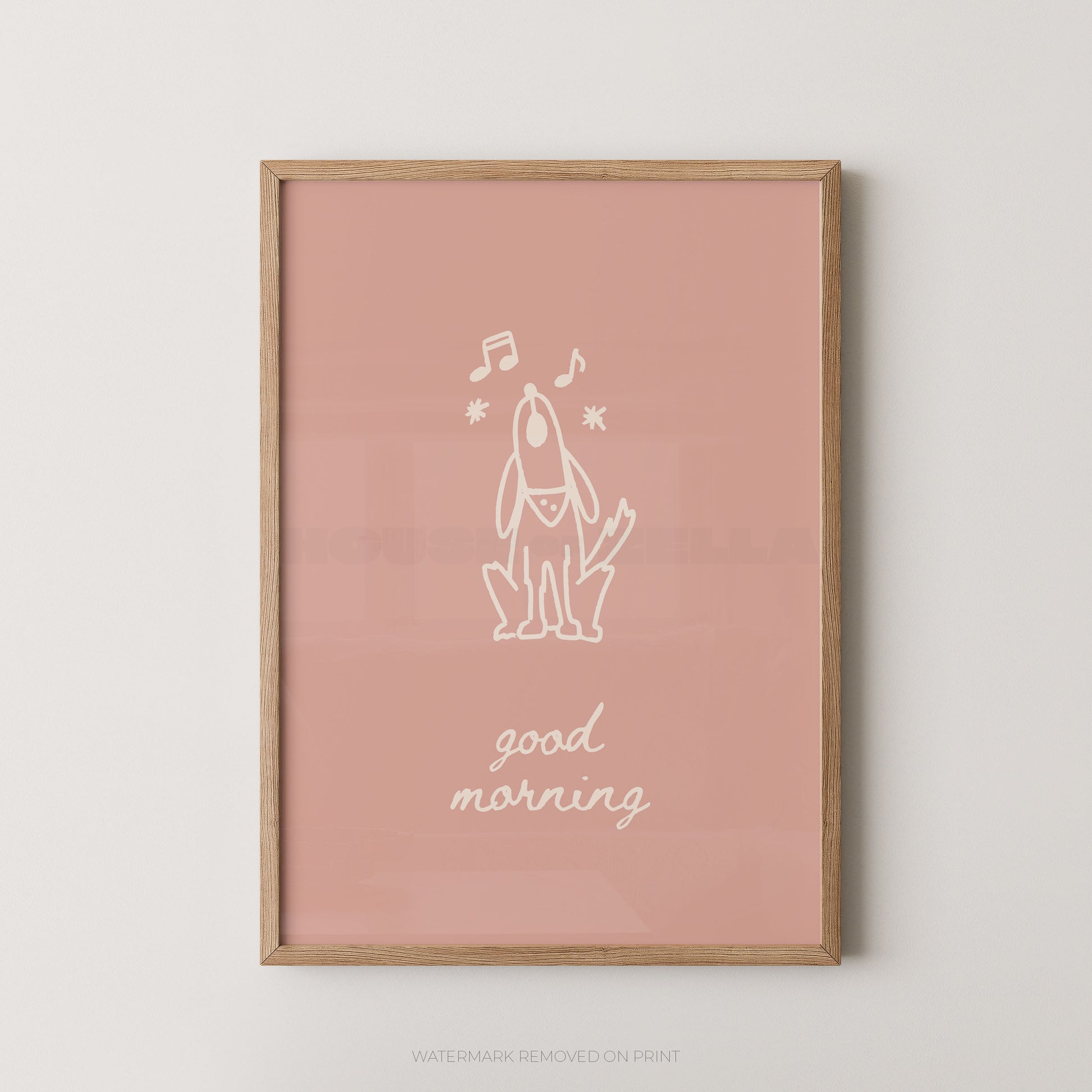 A framed art print featuring a minimalist white line drawing of a dog with musical notes and the text 'good morning' on a dusty pink background, enclosed in a light wood frame.
