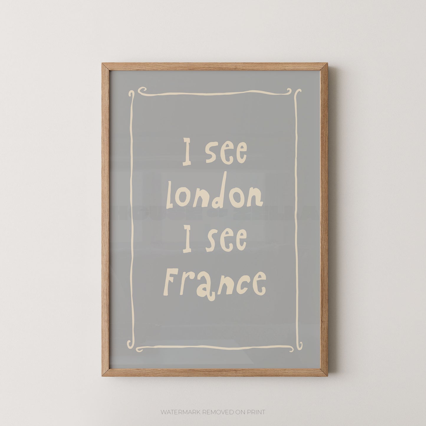 Framed typographic wall art with the text 'I see London I see France' in cream lettering on a muted gray background, enclosed in a light natural wood frame and shown against a white wall.