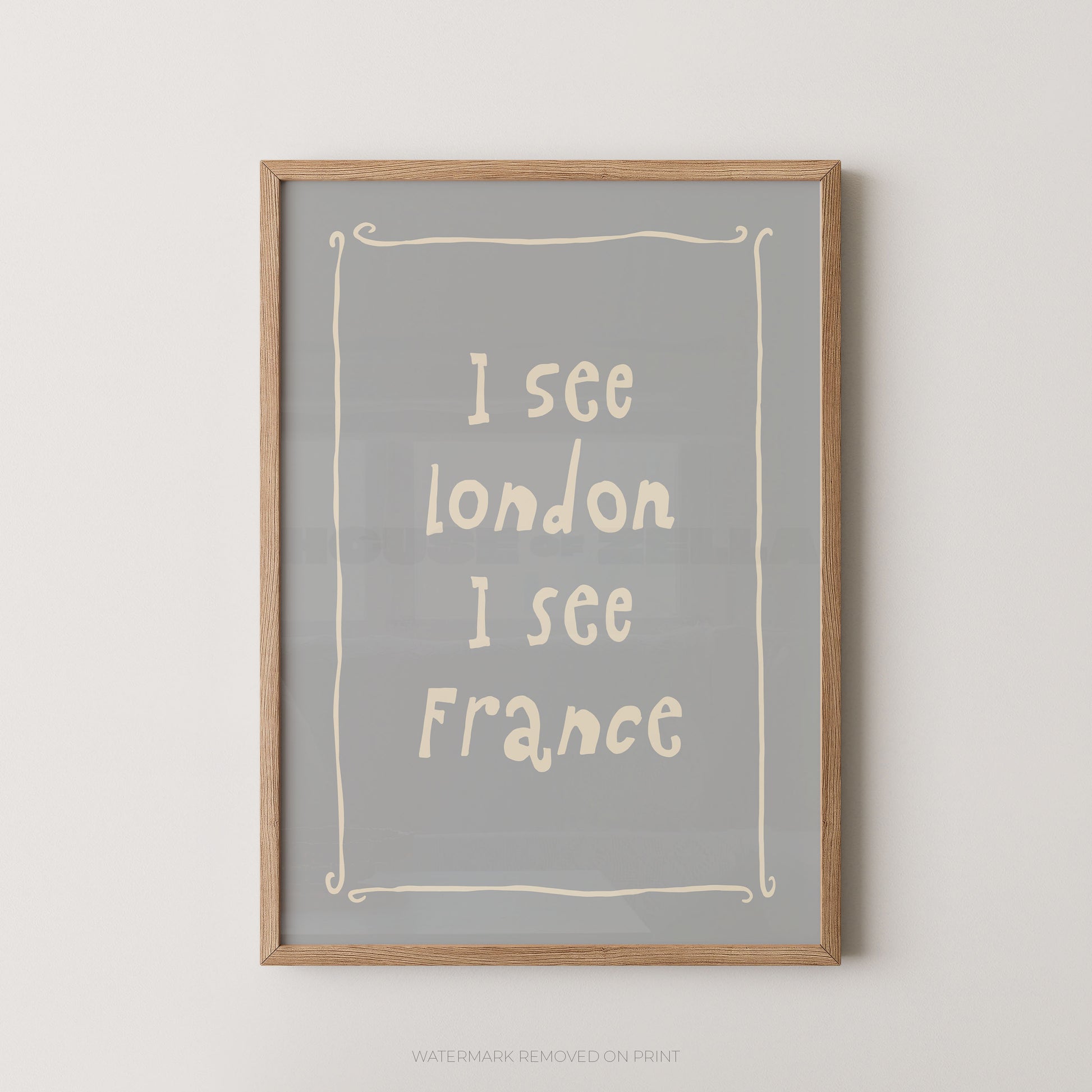 Framed typographic wall art with the text 'I see London I see France' in cream lettering on a muted gray background, enclosed in a light natural wood frame and shown against a white wall.