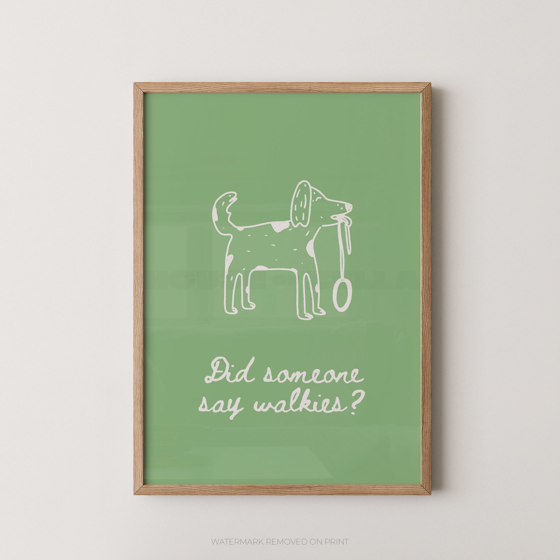 A framed art print featuring a white hand-drawn dog holding a leash on a sage green background, with the text 'Did someone say walkies?' below. The print is housed in a light natural wood frame and is displayed against a neutral light gray wall.