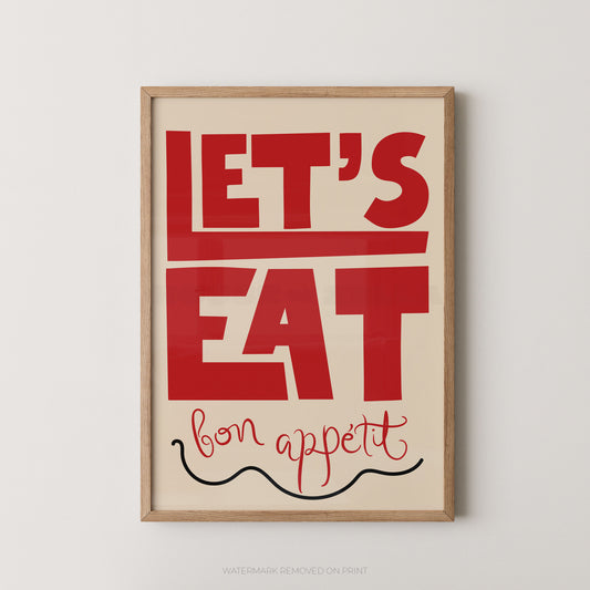 Framed typographic wall art with the words “LET’S EAT” in large red letters on a cream background, with “bon appetit” in red script and a black squiggle line, shown in a light wood frame against a light gray wall.