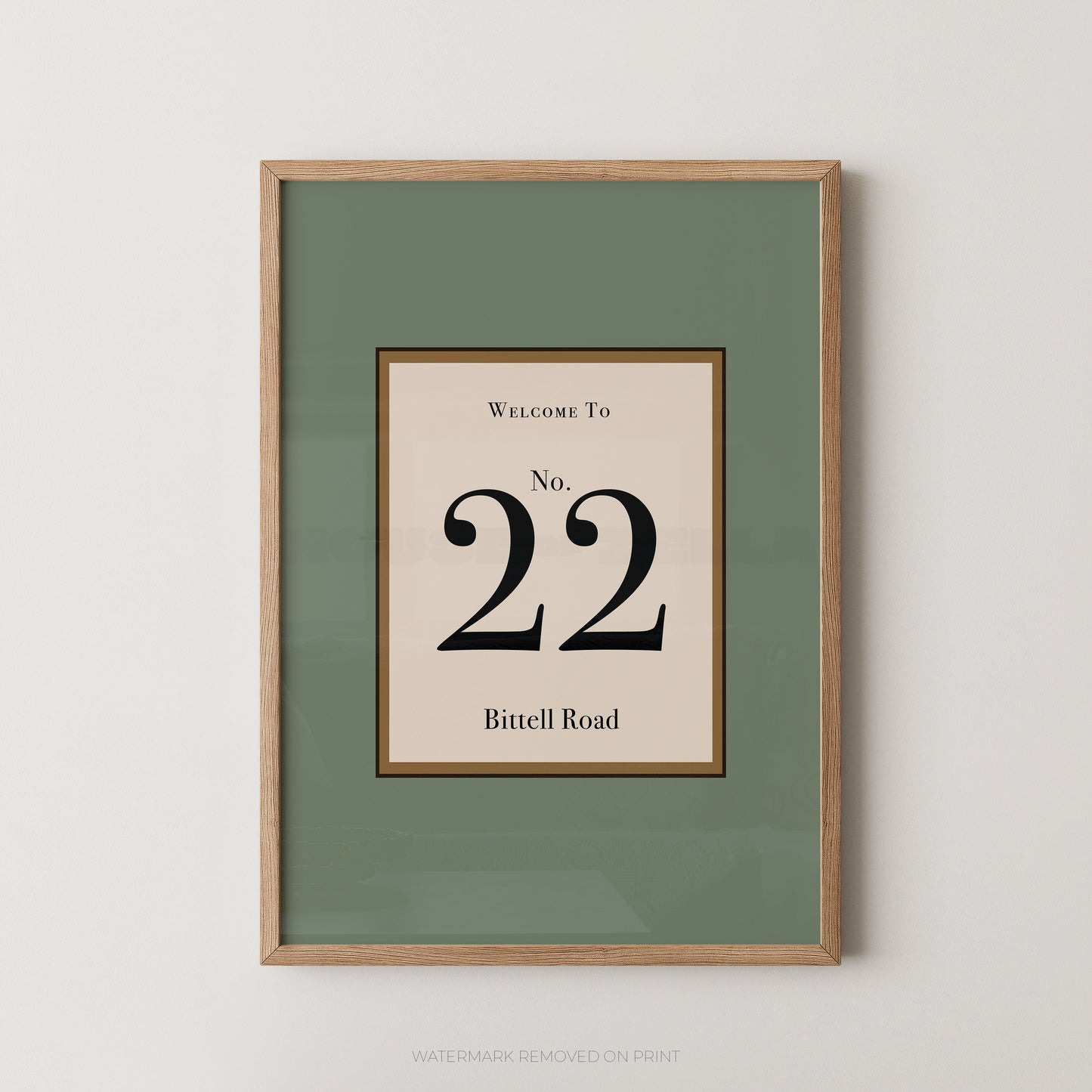 Framed wall art print with a sage green mat and a central cream panel reading 'Welcome To No. 22 Bittell Road' in black serif text, shown in a light wood frame against a light gray wall.