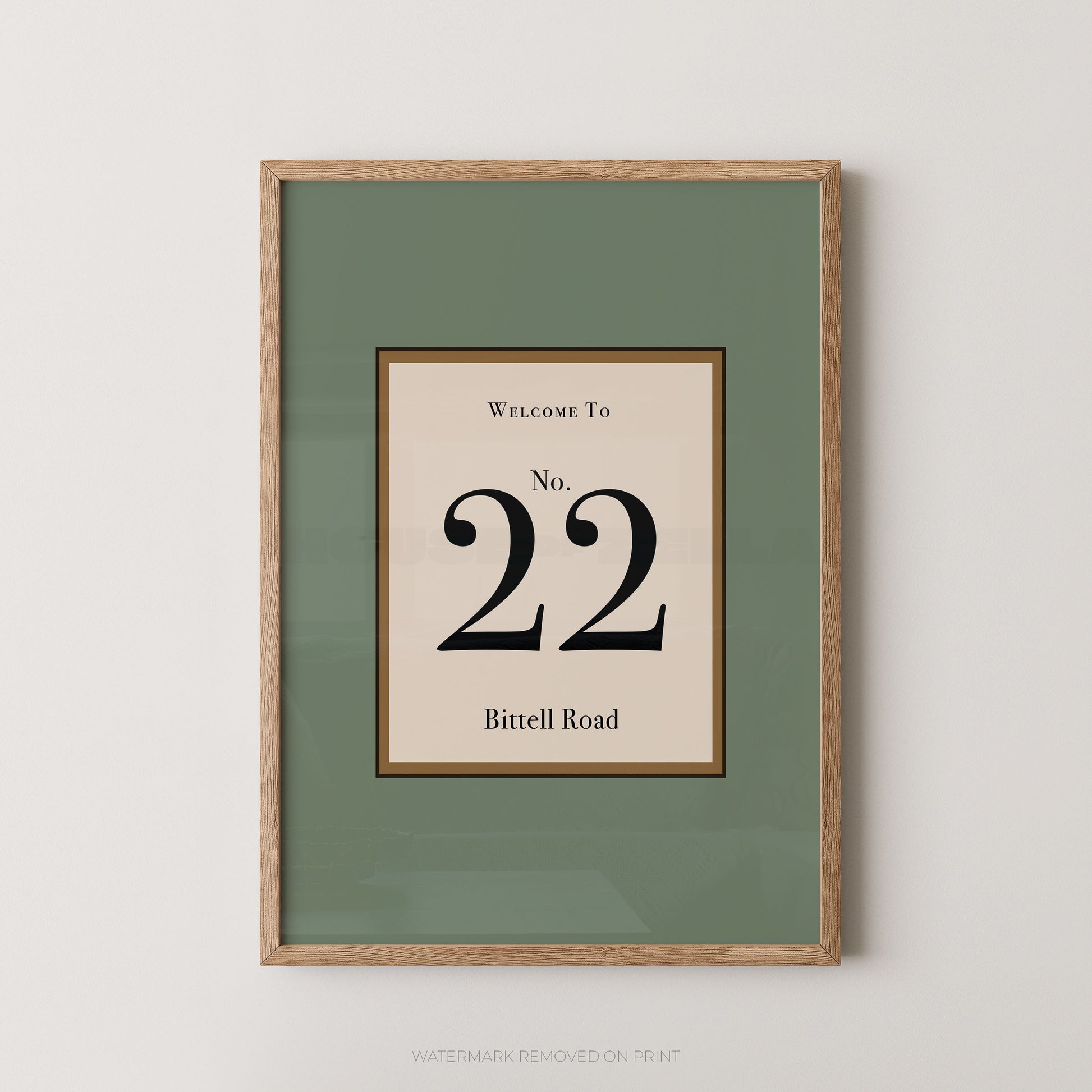 Framed wall art print with a sage green mat and a central cream panel reading 'Welcome To No. 22 Bittell Road' in black serif text, shown in a light wood frame against a light gray wall.