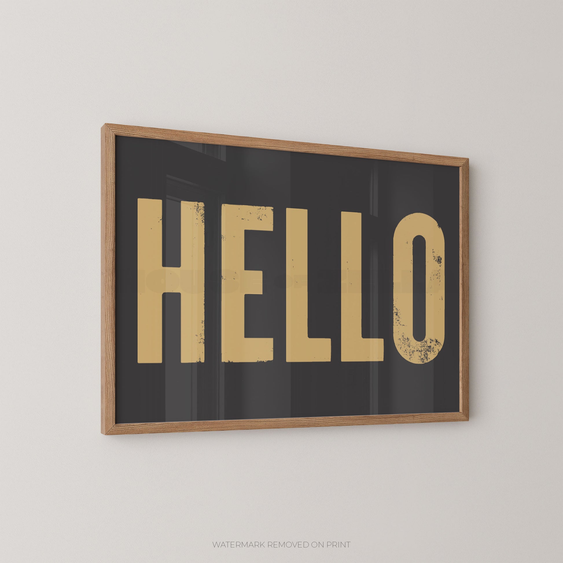 Framed wall art print with the word "HELLO" in large distressed gold letters on a dark charcoal background, shown hanging on a light gray wall.