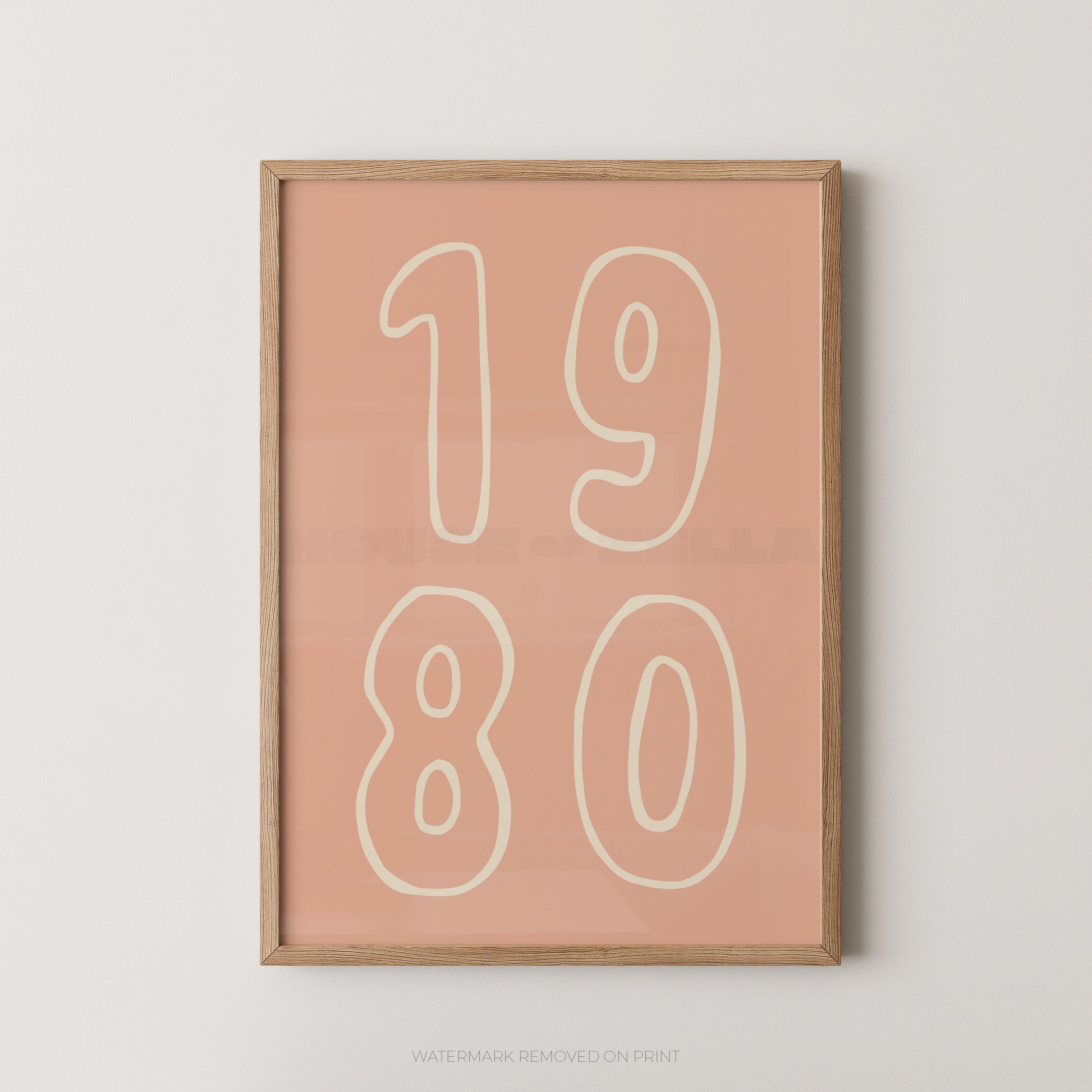 Framed wall art print with the numbers '1980' in cream outlined font on a dusty pink background, shown in a light natural wood frame against a light gray wall.