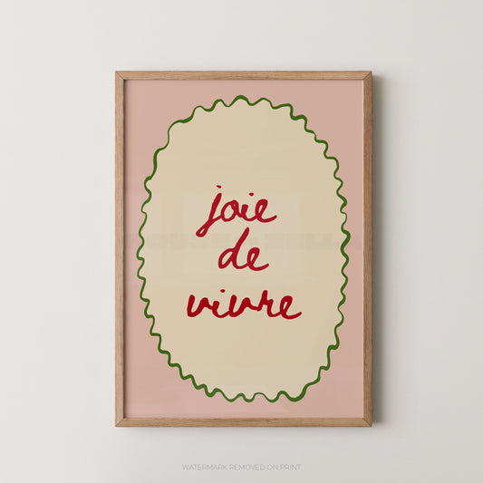 Framed wall art print with the French phrase “joie de vivre” in red script inside a cream oval, bordered by a green wavy line on a dusty pink background, in a light wood frame.