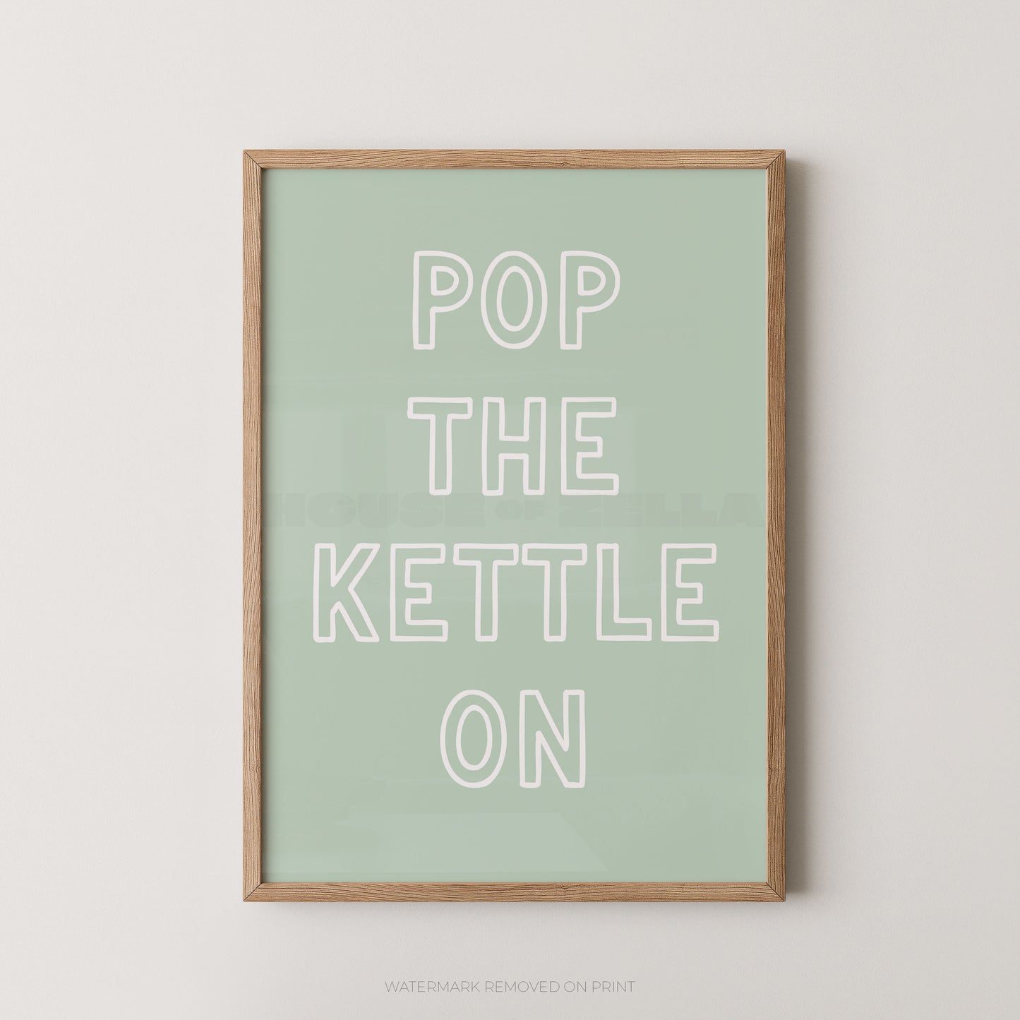 A framed typographic wall art print with the phrase “POP THE KETTLE ON” in white outlined letters on a pale mint green background, shown against a light neutral wall.