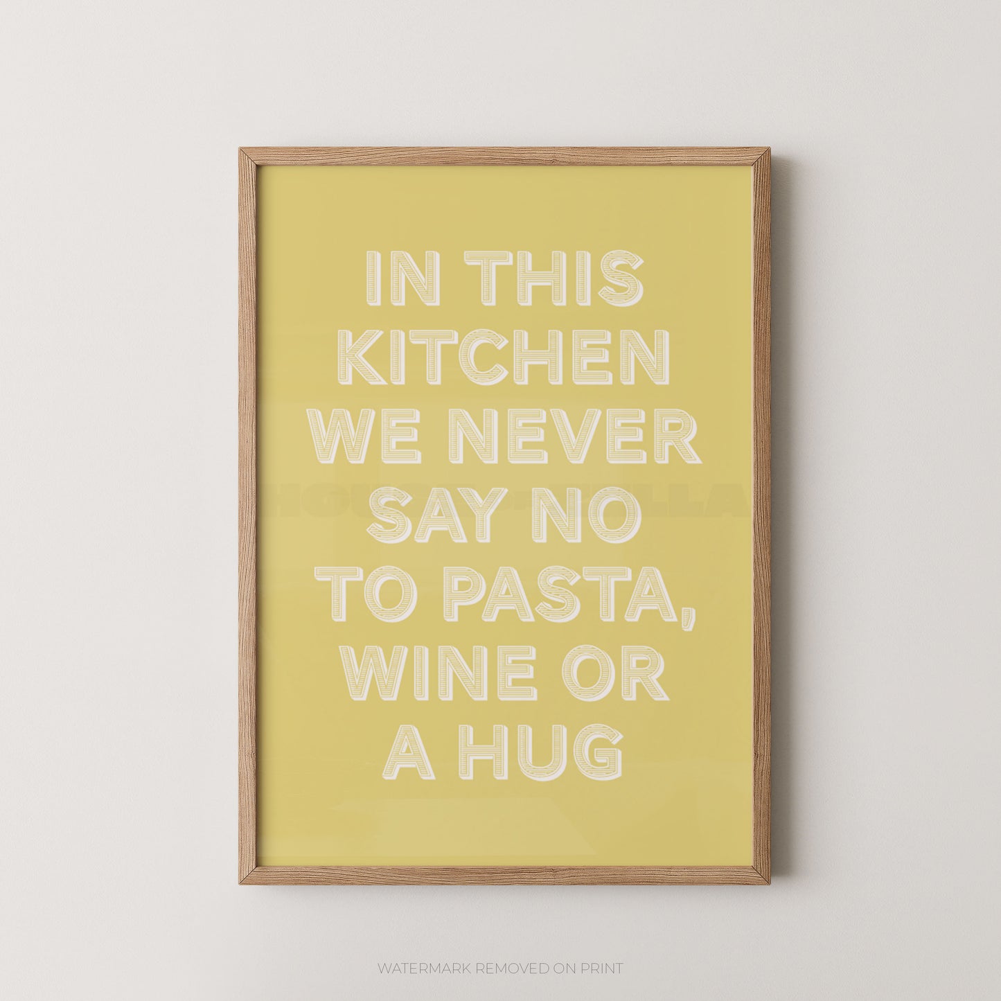 A framed typographic wall art print with a pale yellow background and raised white text reading, 'IN THIS KITCHEN WE NEVER SAY NO TO PASTA, WINE OR A HUG,' shown against a light neutral wall.