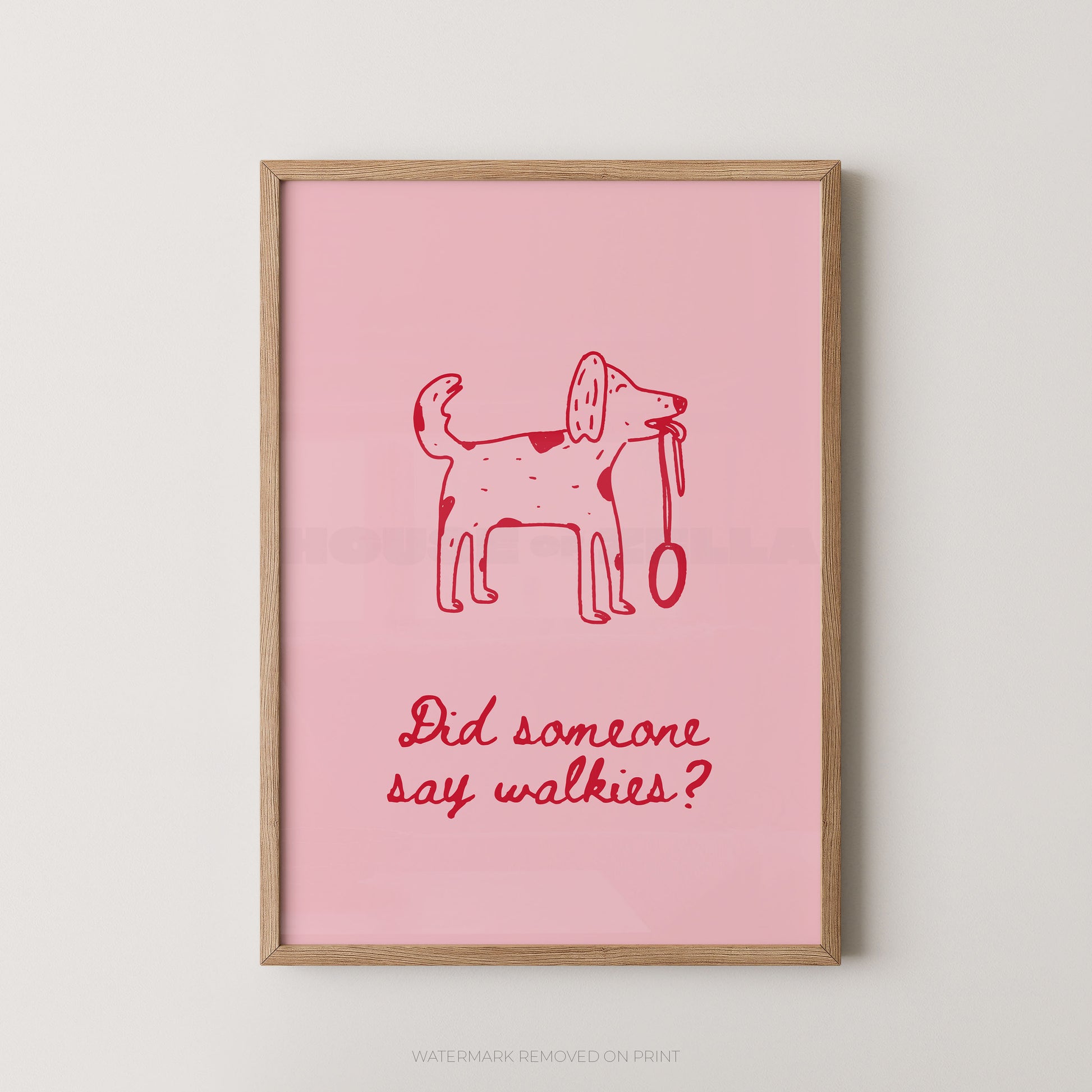 A framed art print featuring a pink background with a red hand-drawn dog holding a leash and the text 'Did someone say walkies?' in red script. The print is housed in a light natural wood frame and is displayed against a neutral light gray wall.