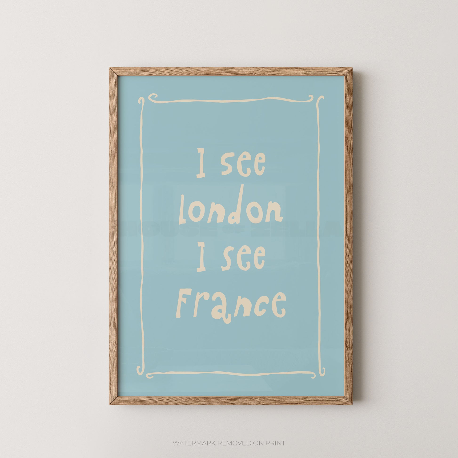 A framed typographic wall art print with a light blue background and cream text reading 'I see London I see France,' enclosed in a natural wood frame against a light neutral wall.