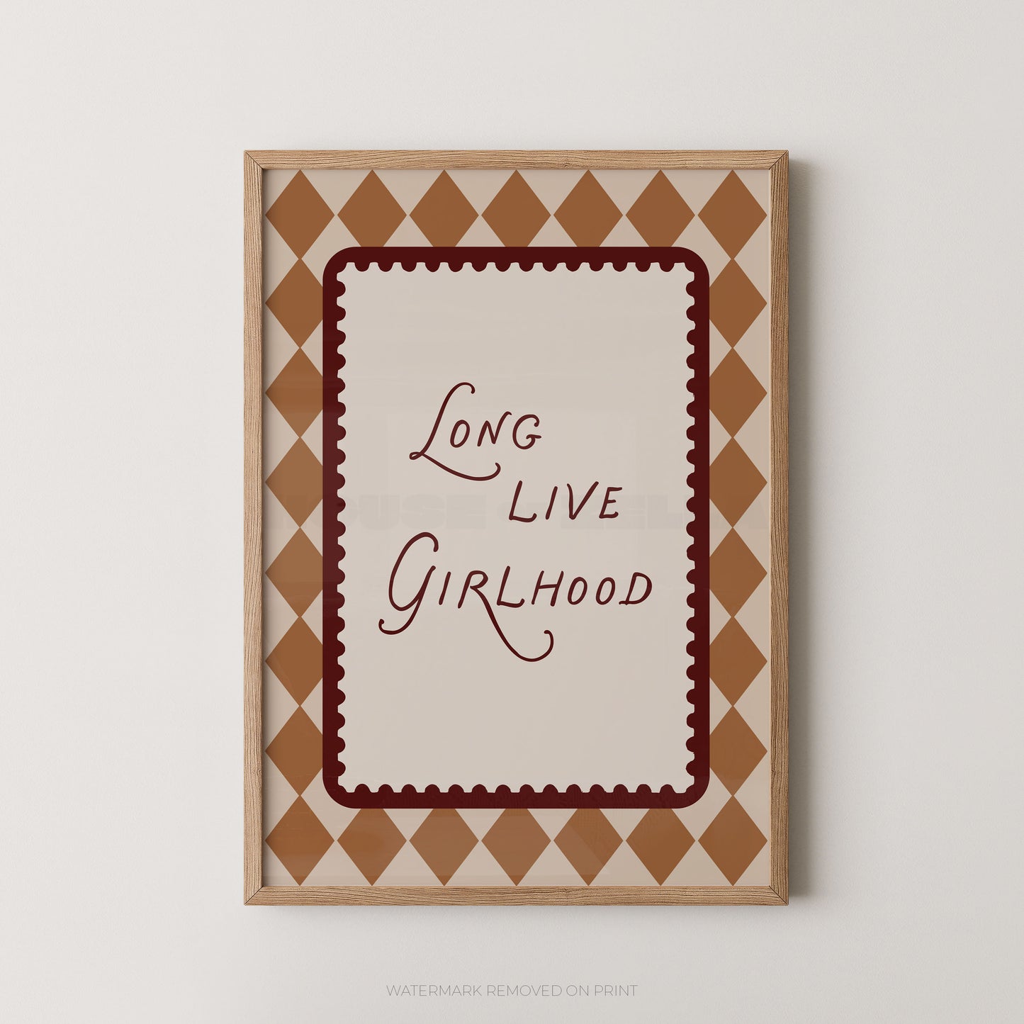 Framed wall art print with the phrase 'Long Live Girlhood' in dark red script inside a scalloped red border, surrounded by a tan and cream diamond pattern, shown against a light gray wall.