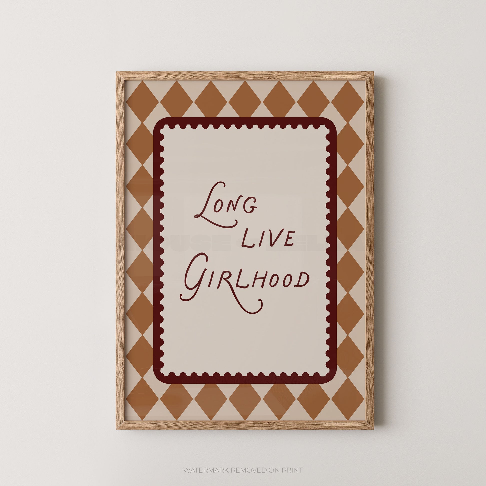 Framed wall art print with the phrase 'Long Live Girlhood' in dark red script inside a scalloped red border, surrounded by a tan and cream diamond pattern, shown against a light gray wall.