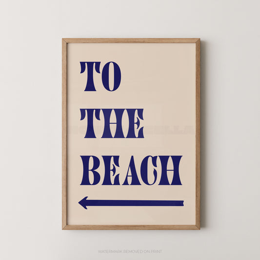 "To The Beach bold typography wall art print with navy blue lettering and a navy left-pointing arrow on a cream background, displayed straight-on in an oak frame"

