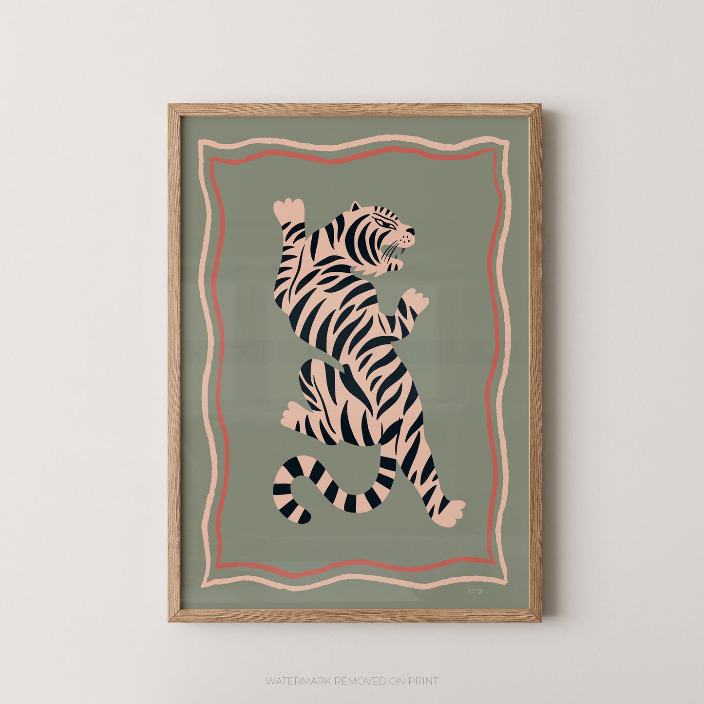 Framed wall art featuring a stylized tiger illustration in black and cream on a muted sage green background, with pink and peach border lines, shown hanging against a light neutral wall.