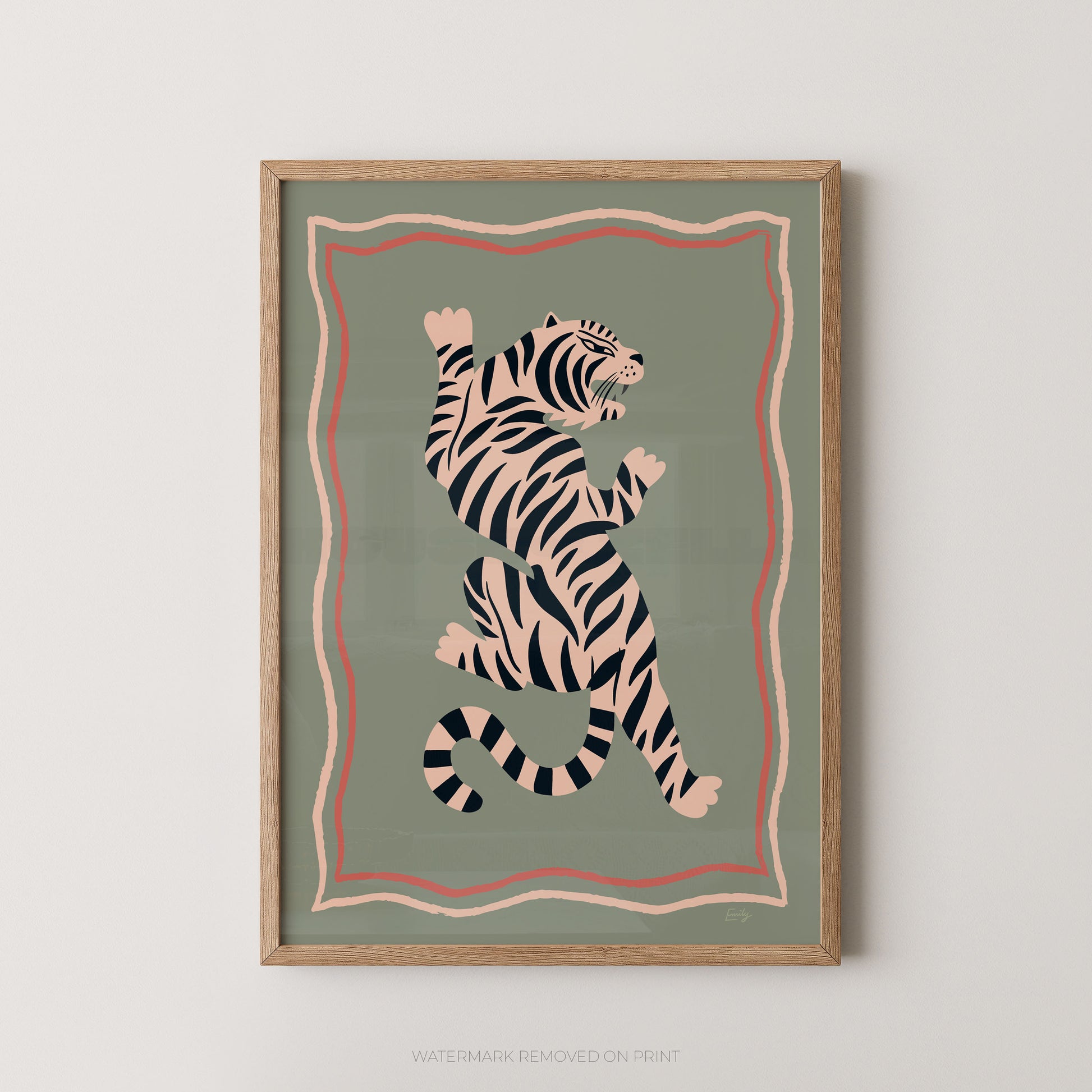 Framed wall art featuring a stylized tiger illustration in black and cream on a muted sage green background, with pink and peach border lines, shown hanging against a light neutral wall.